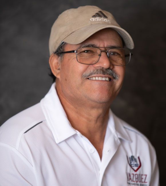 Smiling man in beige cap and glasses wearing a white polo shirt against a dark backdrop