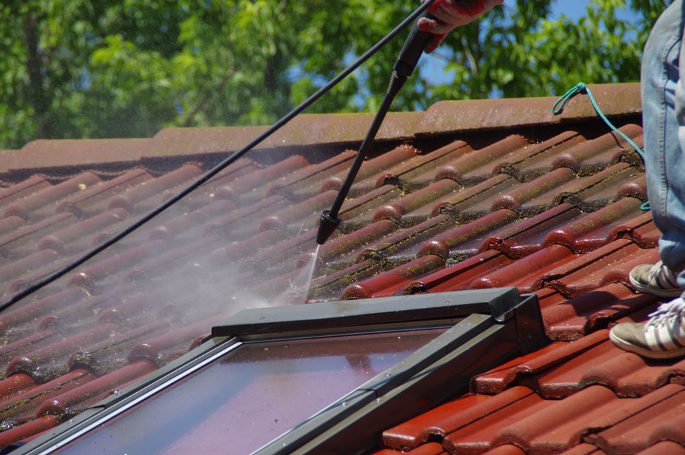 A Person is Cleaning a Roof With a High Pressure Washer — DJ's Pressure Cleaning In Mission Beach, QLD
