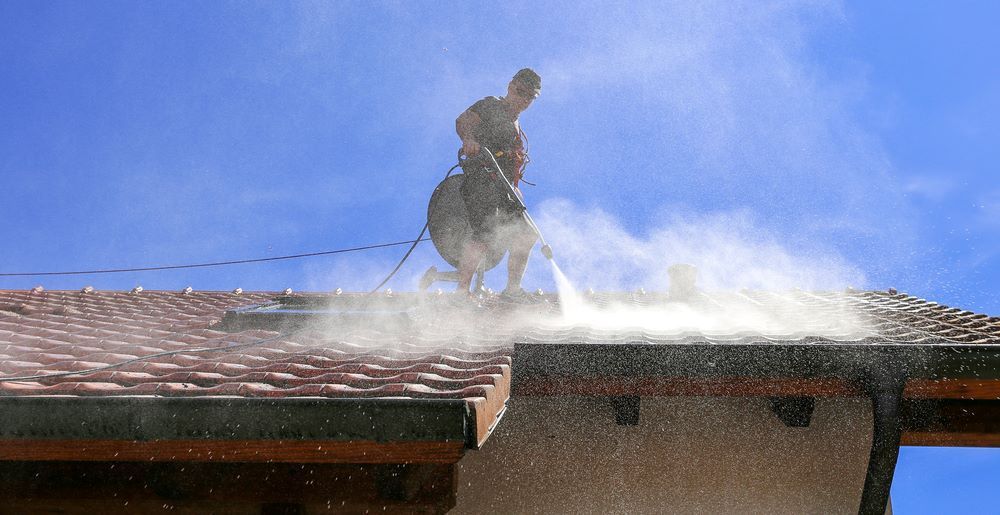 A Man is Cleaning the Roof of a House With a High Pressure Washer — DJ's Pressure Cleaning In Cardwell, QLD