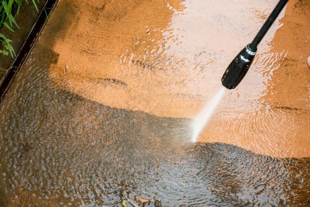 A Person is Using a High Pressure Washer to Clean a Concrete Surface — DJ's Pressure Cleaning In Cardwell, QLD