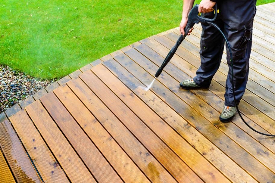 A Man is Cleaning a Wooden Deck With a High Pressure Washer — DJ's Pressure Cleaning In Carruchan, QLD