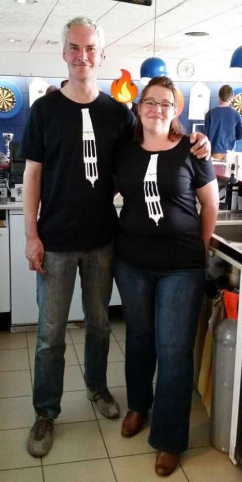 Twee personen in bijpassende zwarte T-shirts met een witte opdruk, in een bar of café.