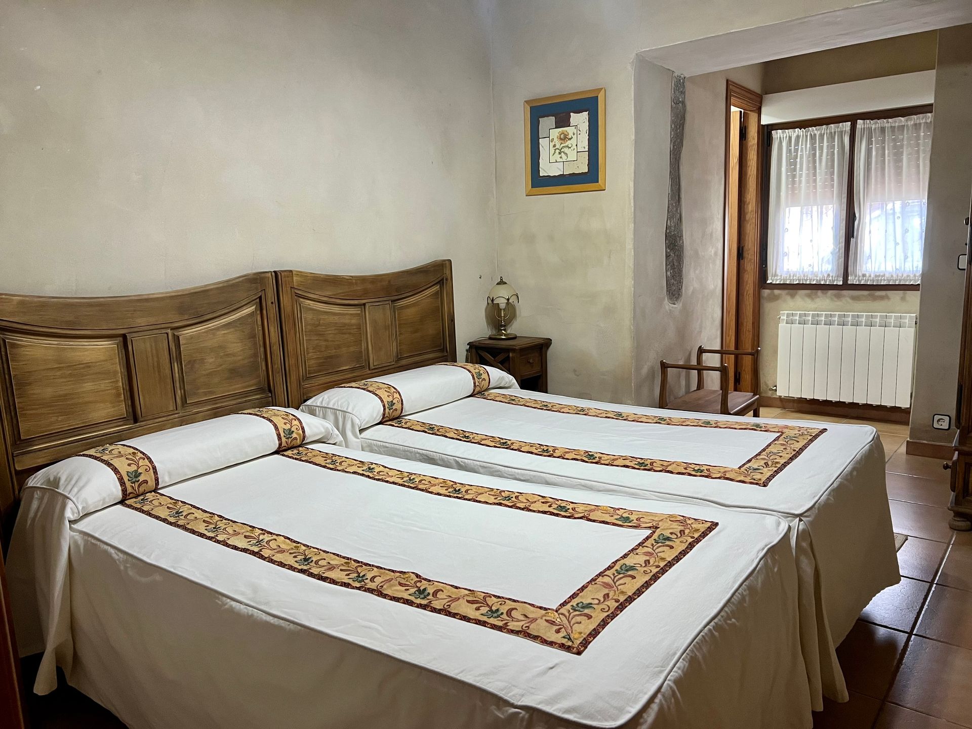 Bedroom with two neatly made twin beds, wooden headboards, and a window with sheer curtains.