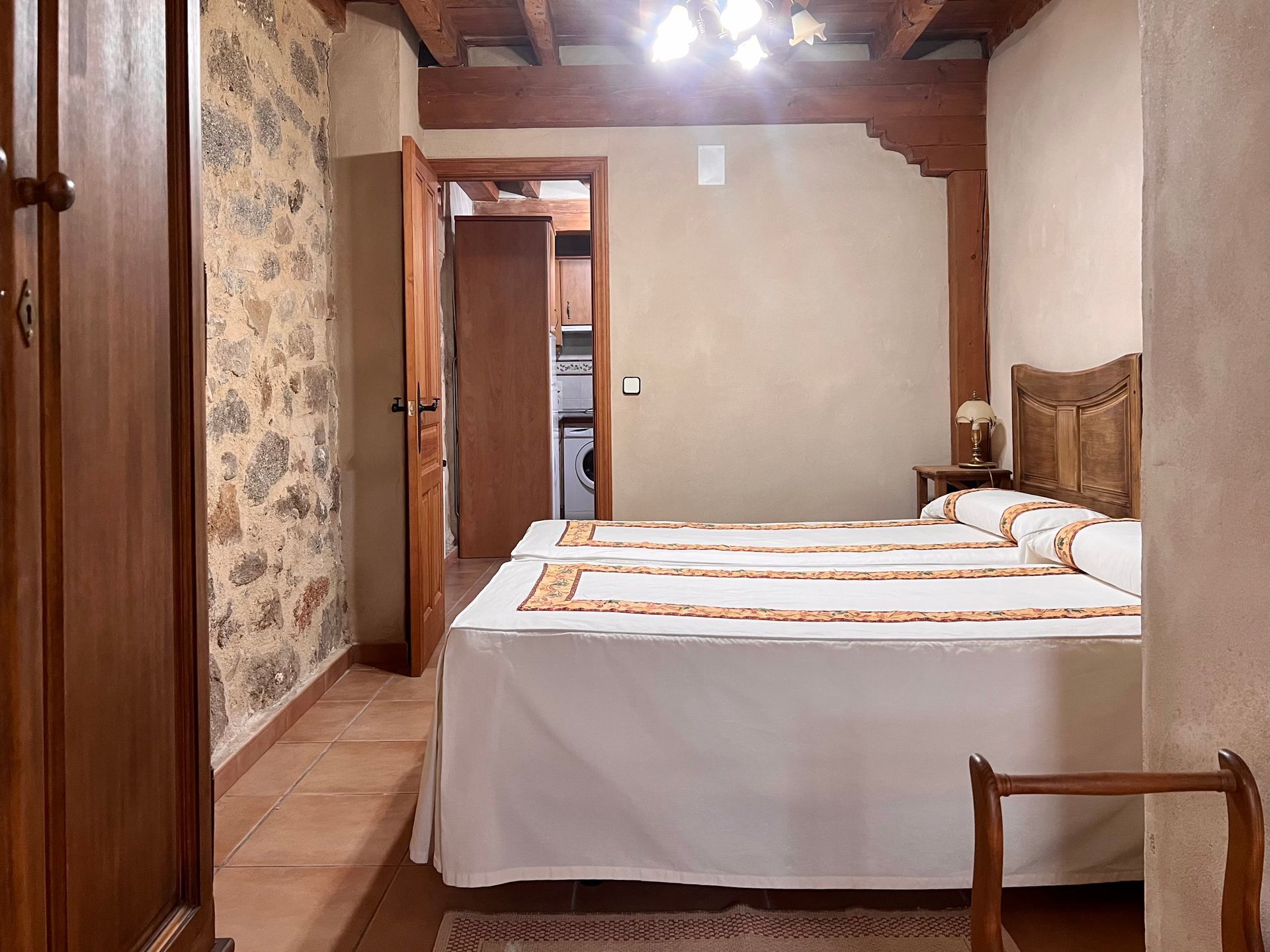 Cozy bedroom with two neatly made twin beds, wood beams, and a floral wall tapestry