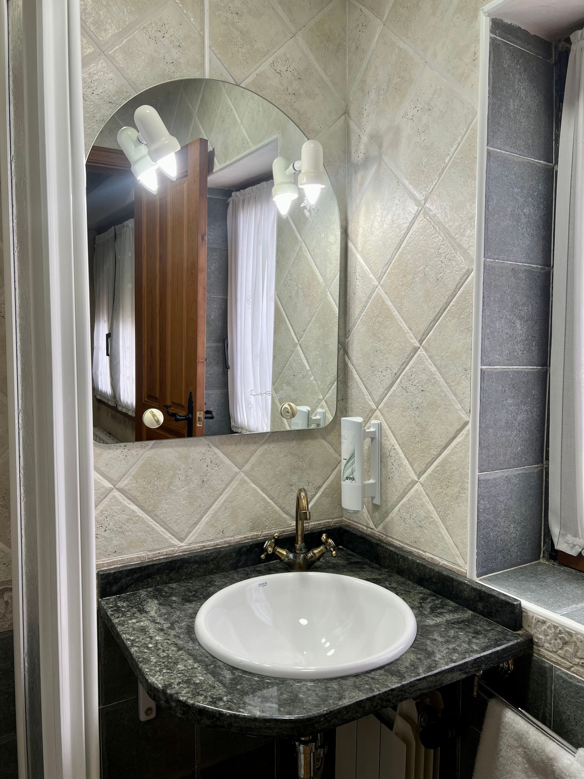 Bathroom vanity with round sink, black countertop, arched mirror, and tiled walls