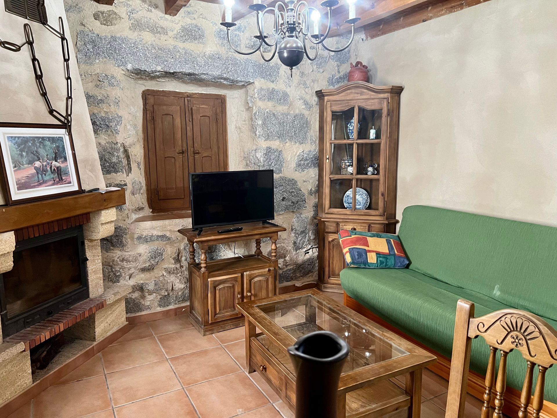 Cozy rustic living room with fireplace, TV, wood cabinet, green sofa, and terracotta tile floor