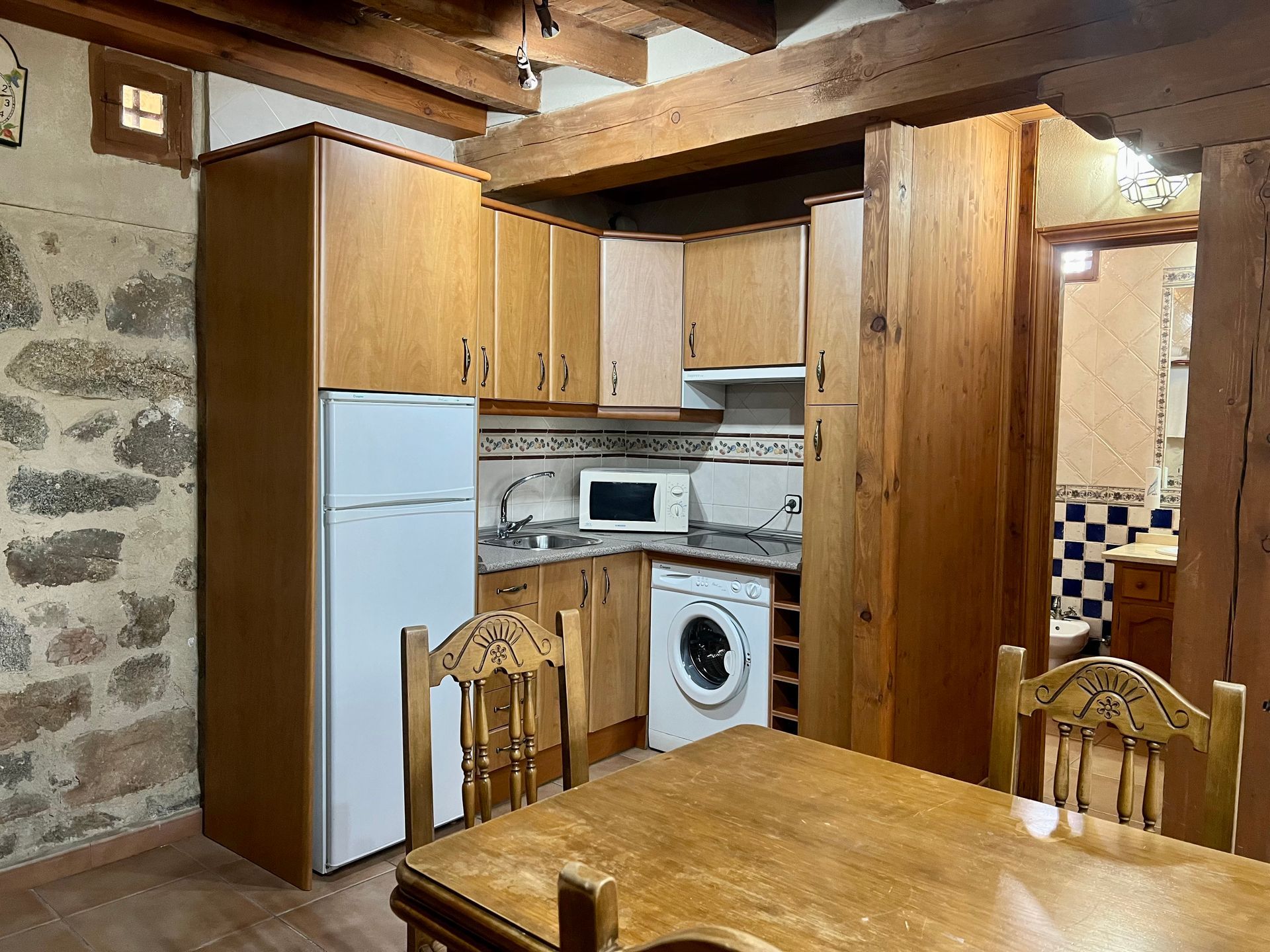 Rustic kitchen with wooden cabinets, white appliances, stone wall, and a dining table in the foreground