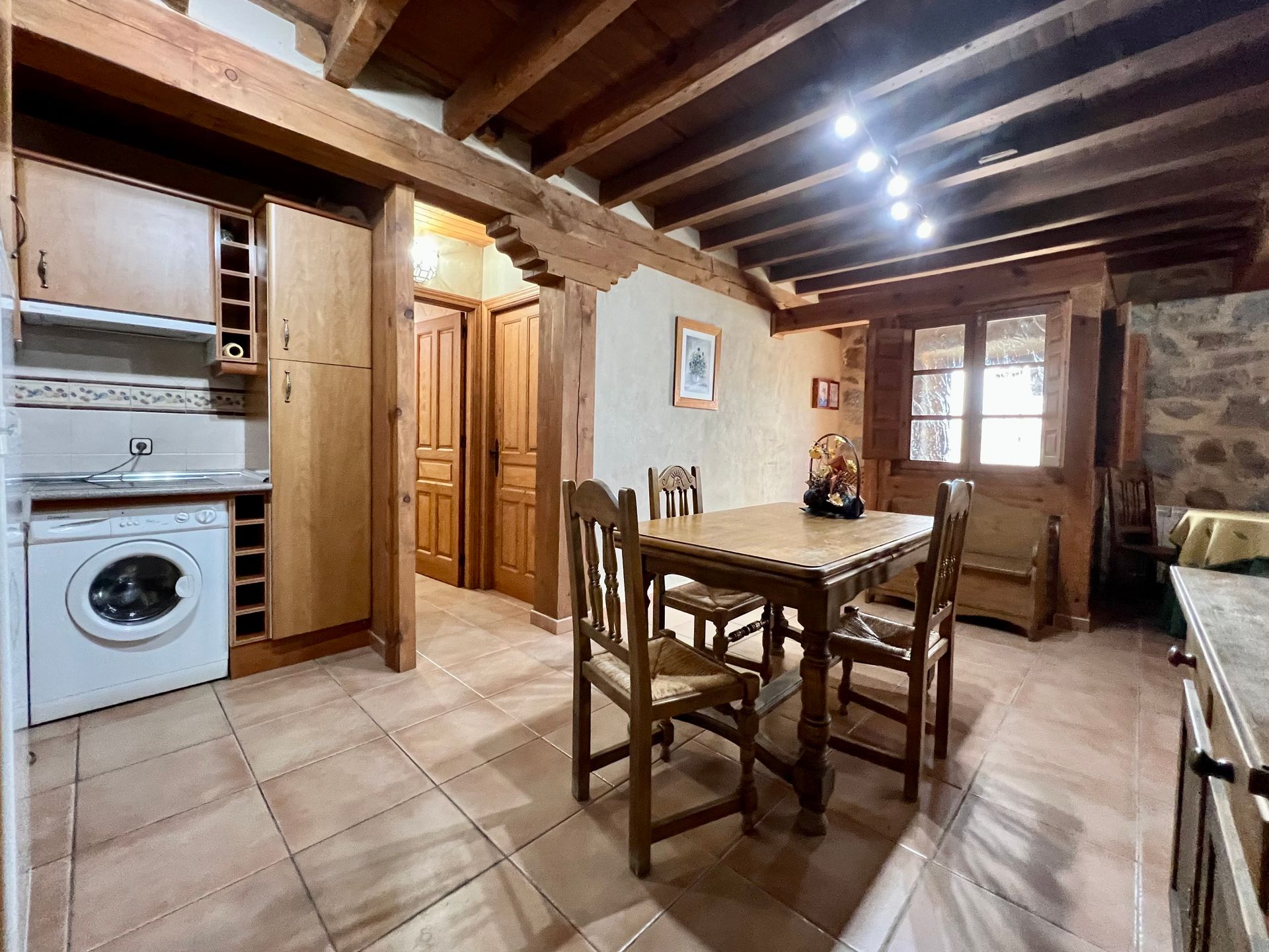 Rustic kitchen and dining area with wooden beams, tiled floor, table, chairs, and washing machine