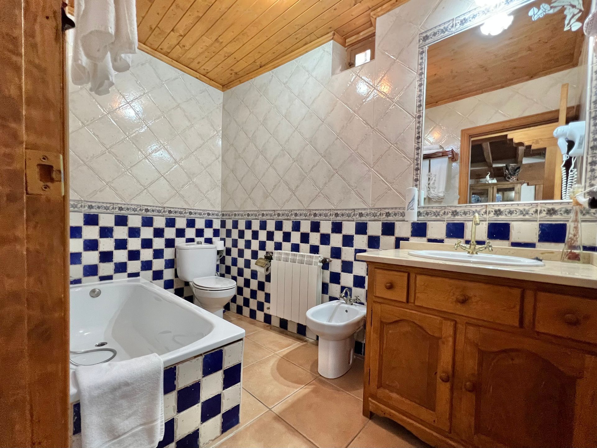 Bathroom with blue-and-white tile, bathtub, toilet, and wooden vanity under a sloped wood ceiling