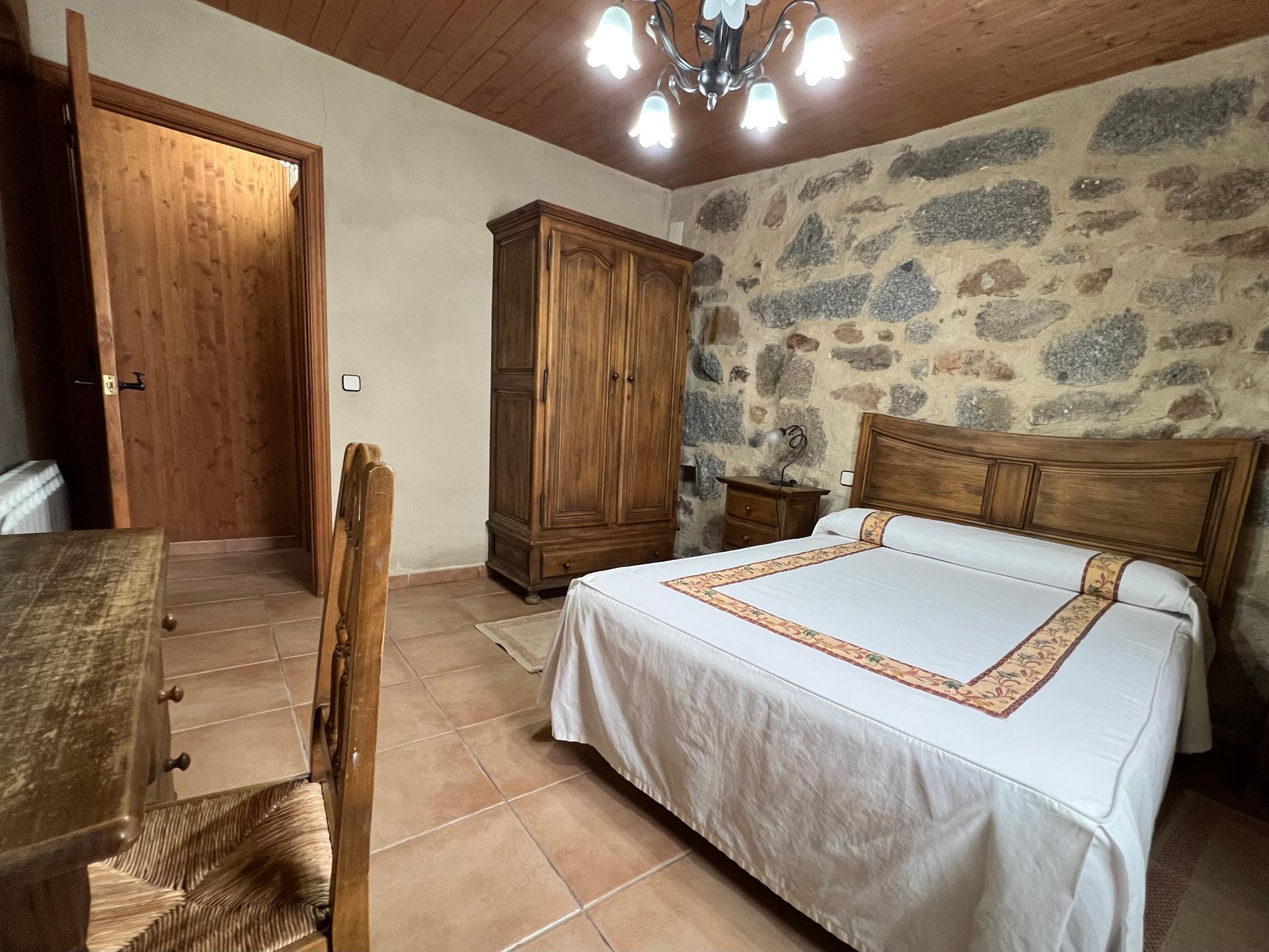 Rustic bedroom with stone accent wall, wooden bed, wardrobe, and open door