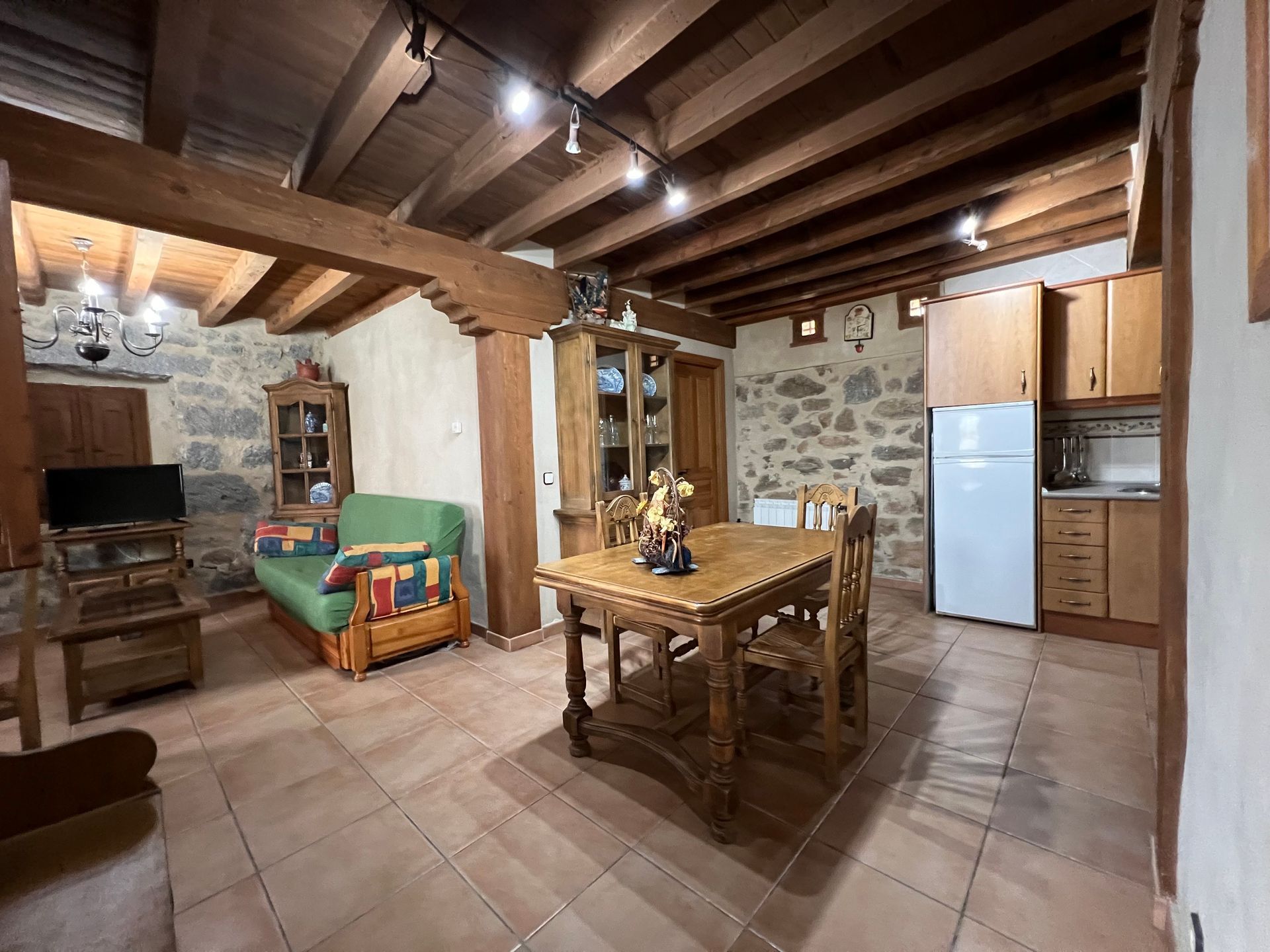 Rustic kitchen-dining room with wooden beams, tiled floor, table, chairs, and refrigerator