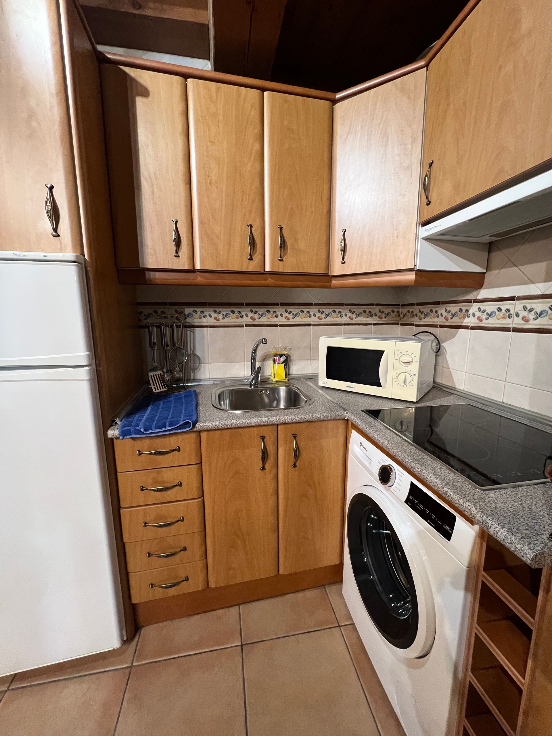 Small kitchen with wood cabinets, white appliances, black stovetop, and a microwave on the counter.