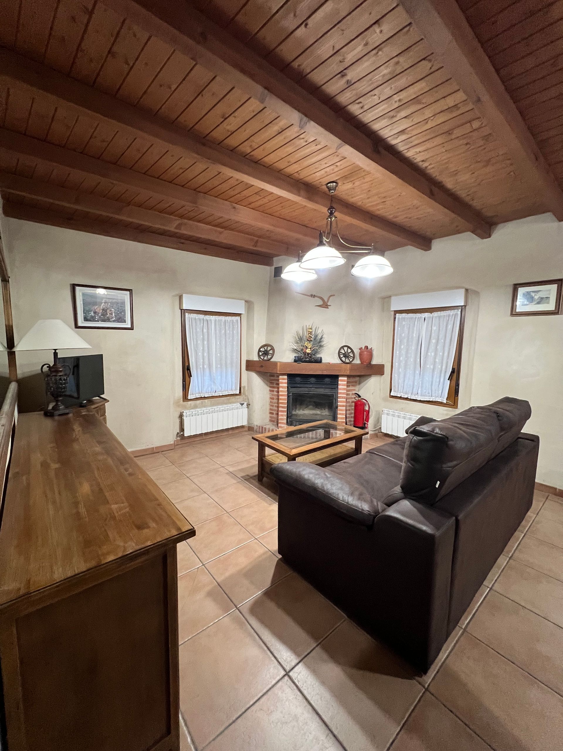 Cozy living room with wood ceiling, fireplace, tiled floor, and dark sofa facing the hearth