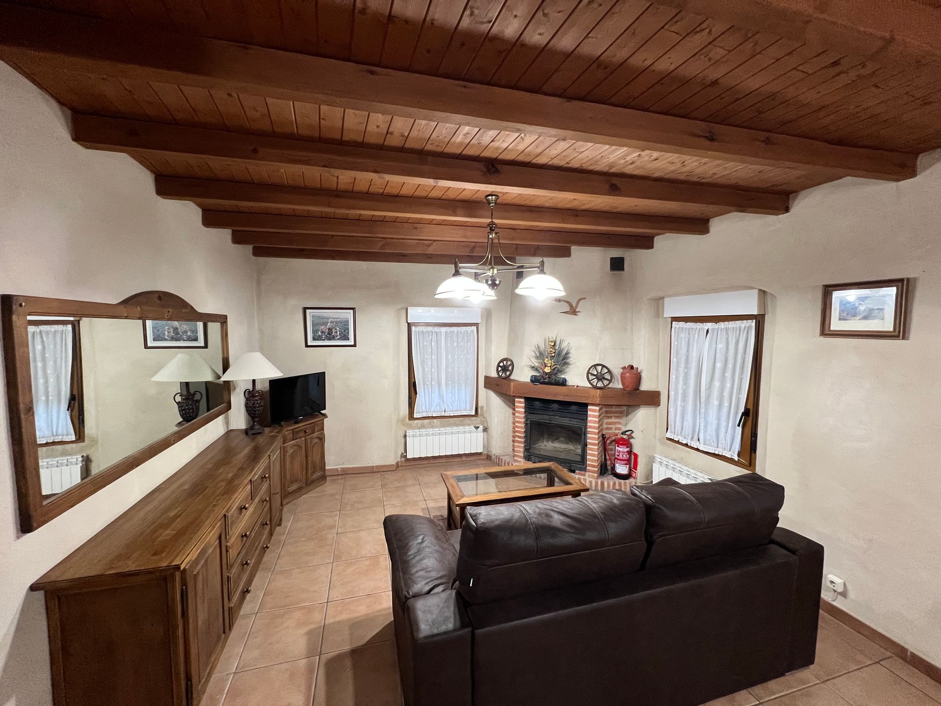 Cozy living room with wood-beamed ceiling, dark sofa, fireplace, and large mirror on the left wall