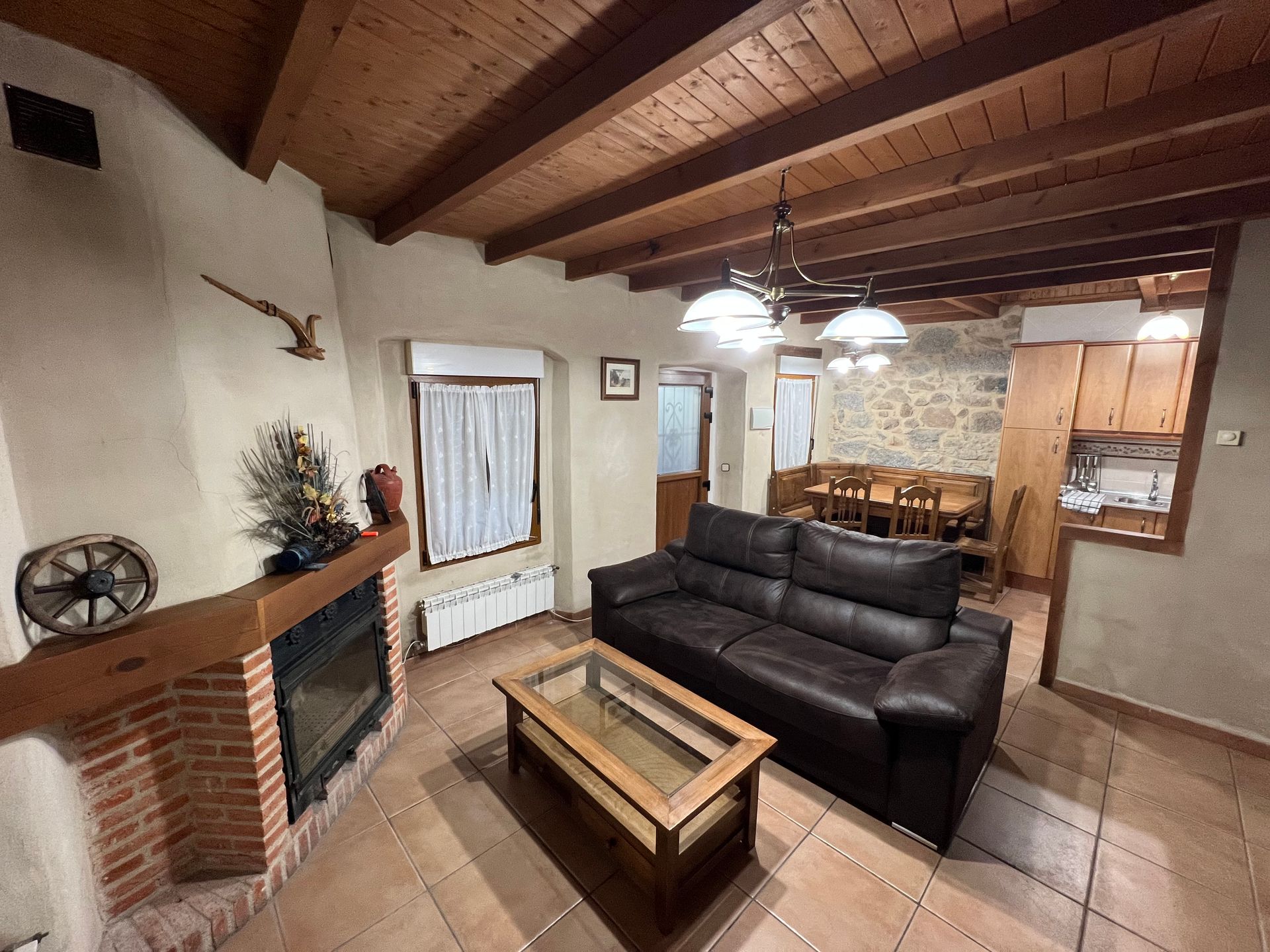 Cozy living room with leather sofa, coffee table, brick fireplace, tiled floor, and wood-beamed ceiling