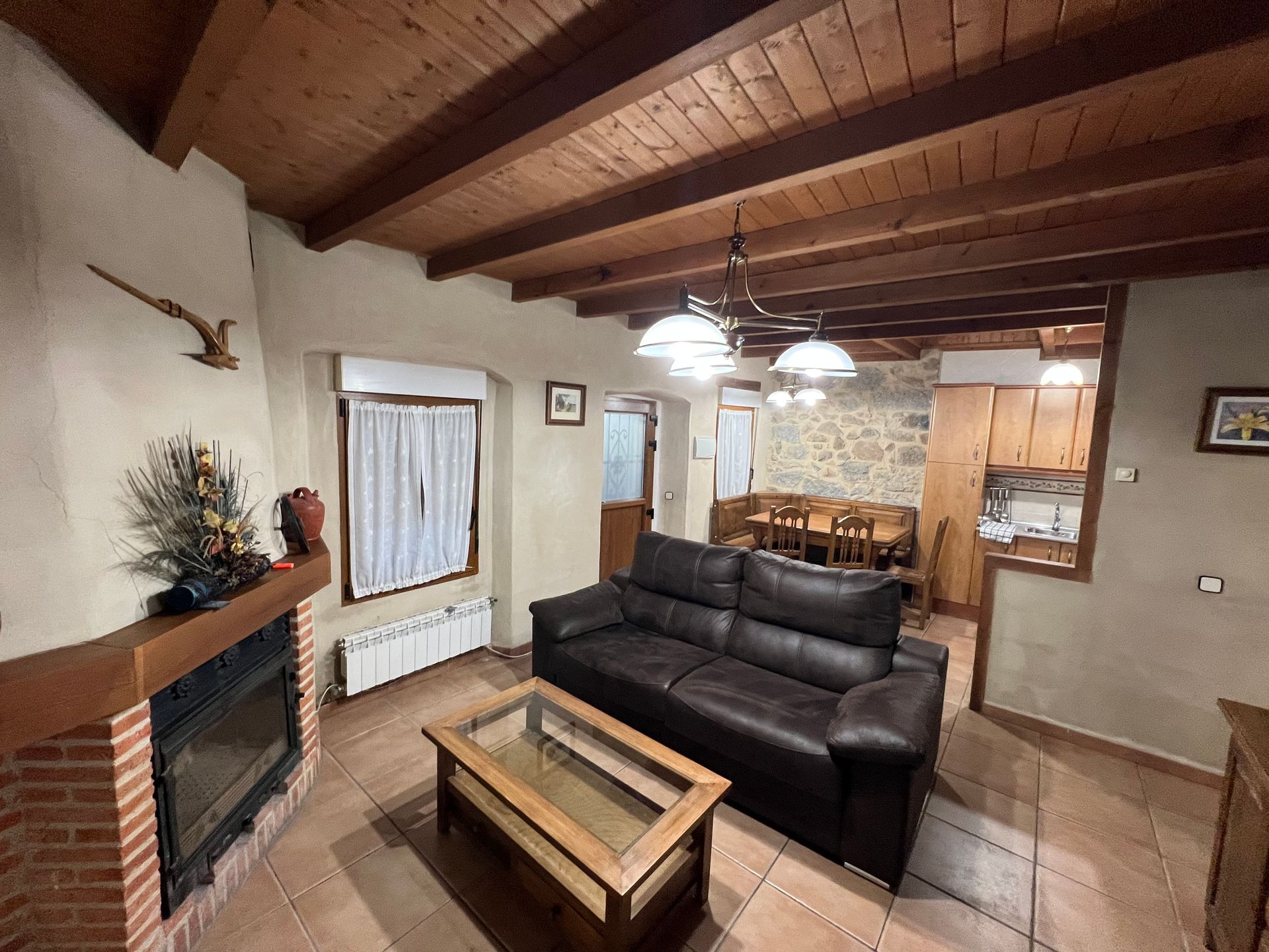 Cozy living room with wood ceiling, black sofa, coffee table, fireplace, and dining area in back