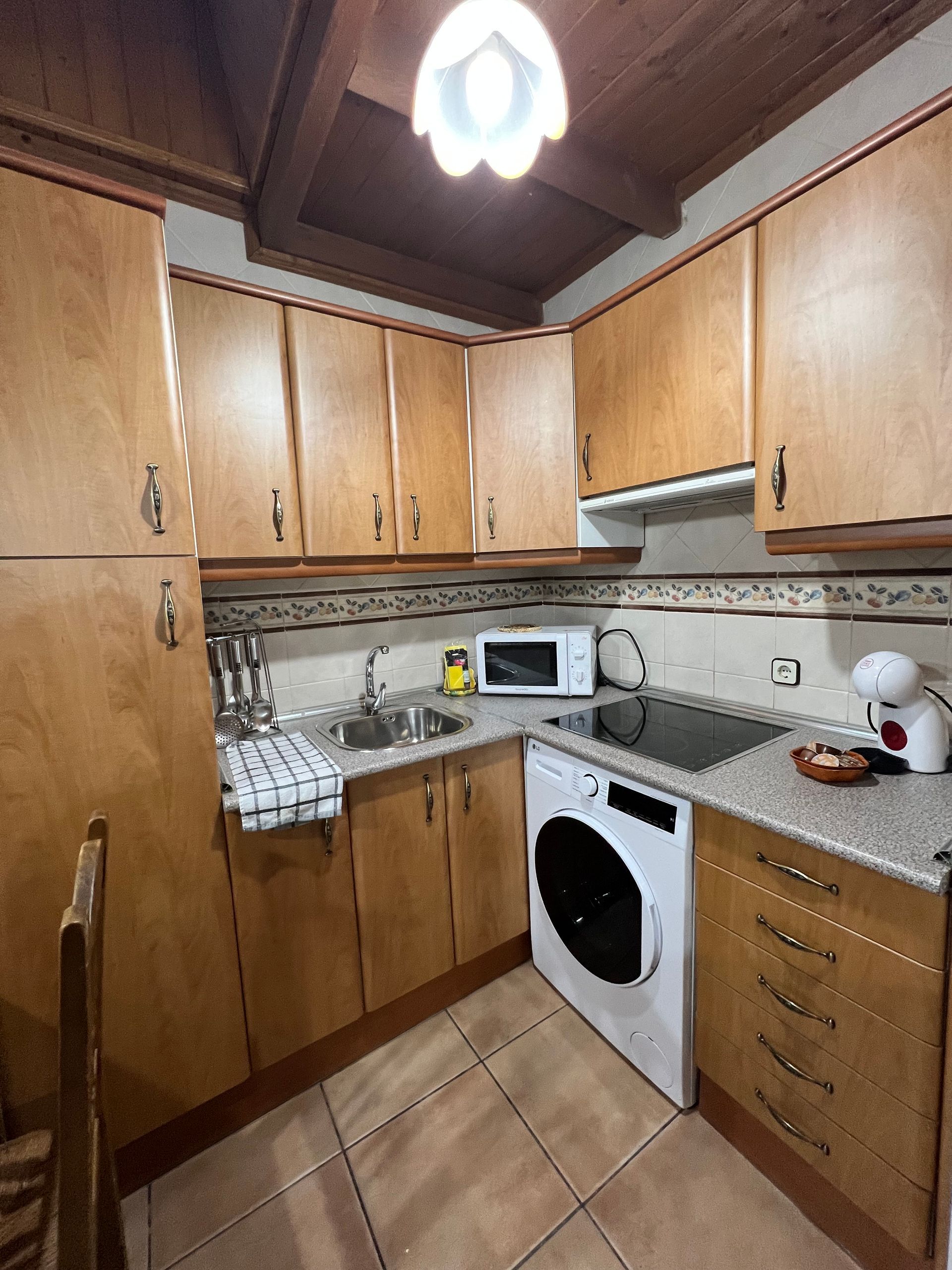 Small kitchen with wooden cabinets, tiled floor, white appliances, and a countertop microwave.