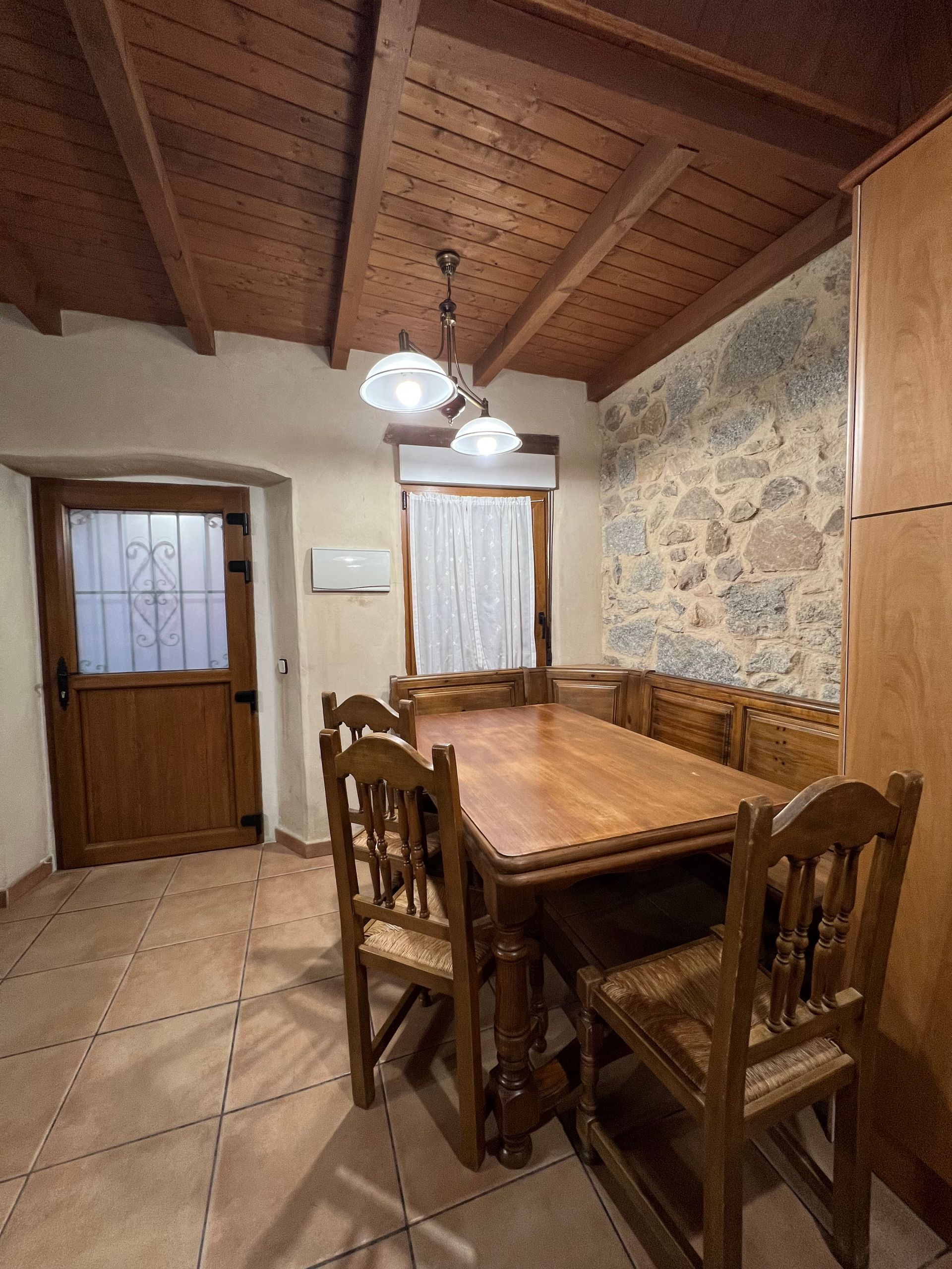 Rustic dining room with wooden table and chairs, stone accent wall, and hanging pendant lights