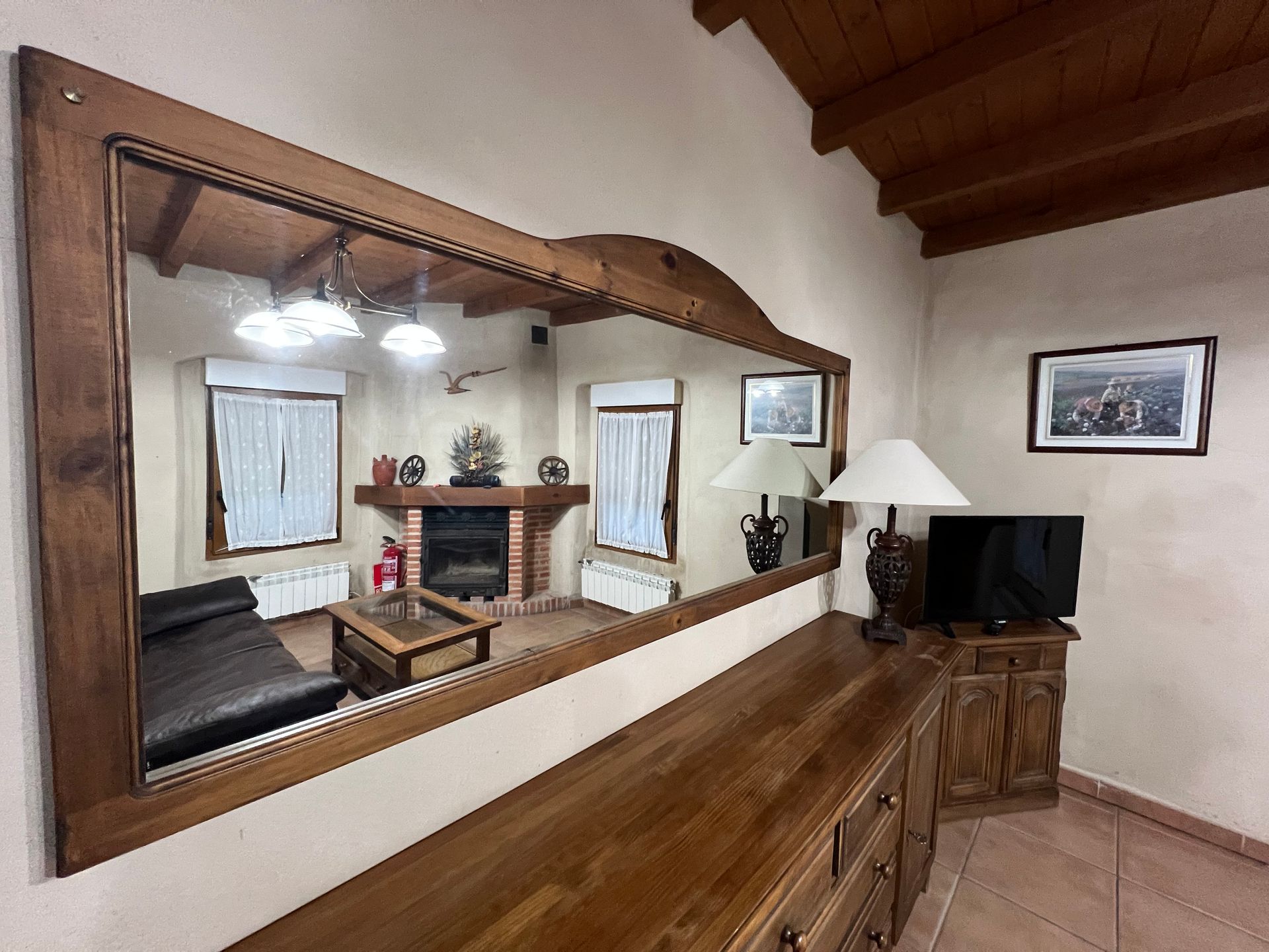 Living room with a large wall mirror, wood dresser, fireplace, TV, and framed wall art