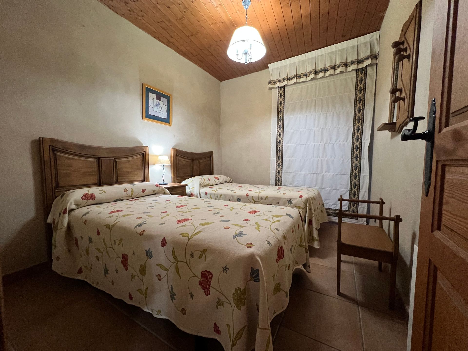 Bedroom with two twin beds, floral bedspreads, wooden headboards, and a window with curtains.