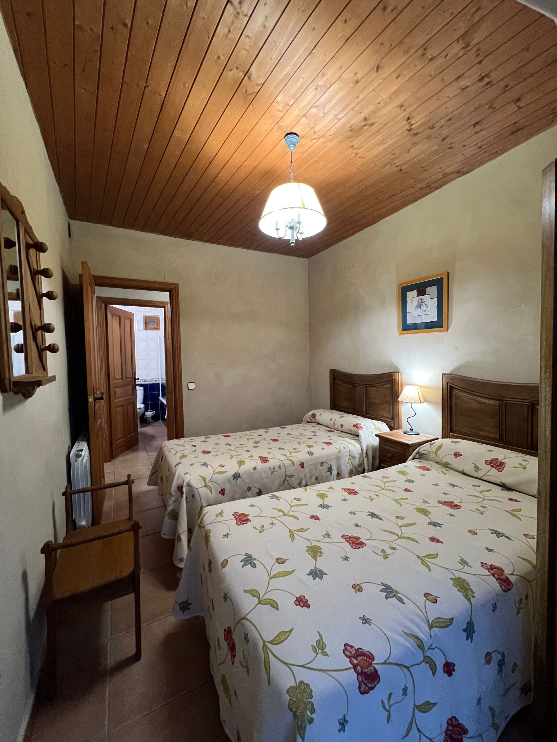 Cozy bedroom with two twin beds, floral bedding, wood-paneled ceiling, and a hanging light.