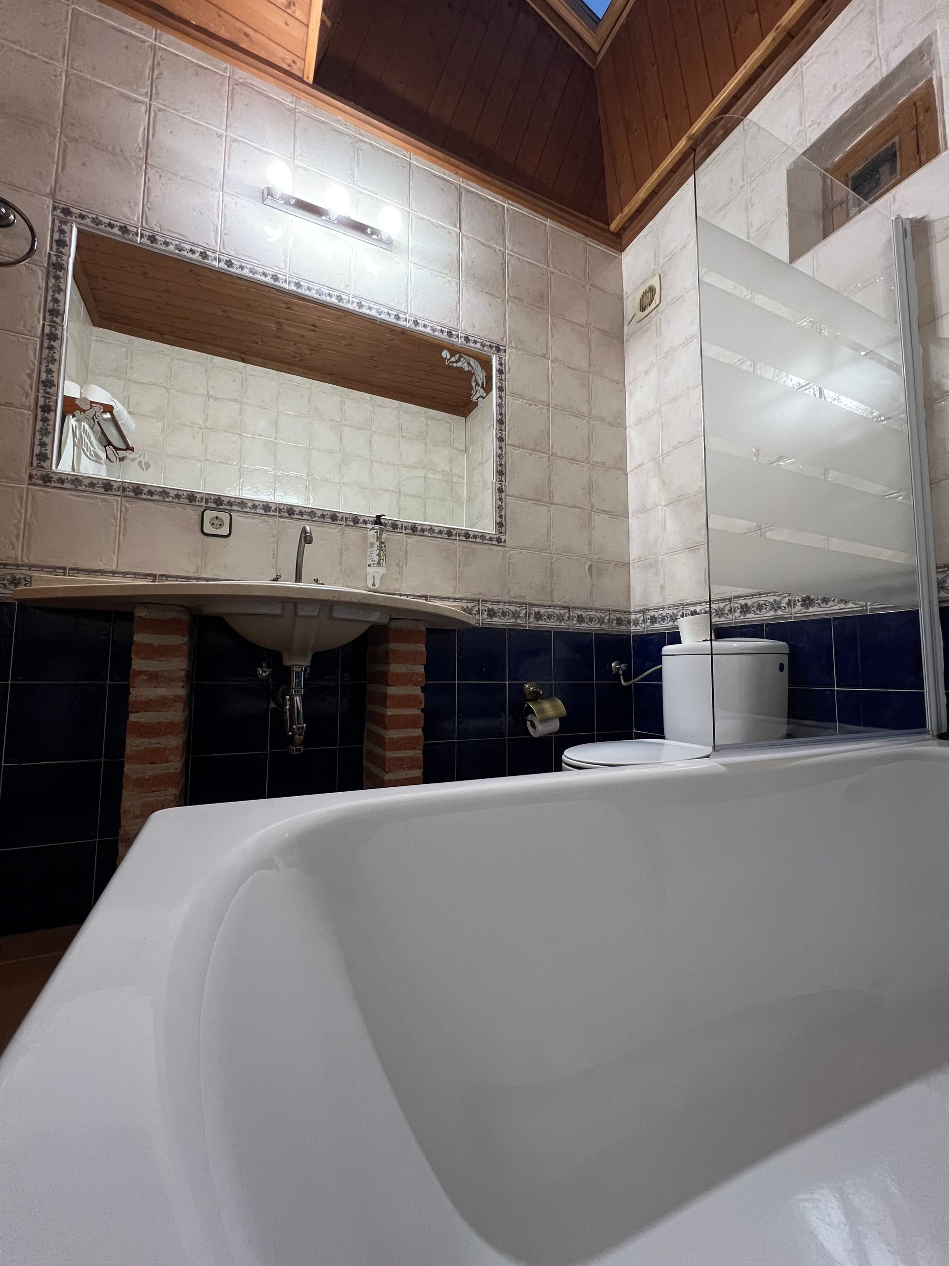 Modern bathroom with a white tub, tiled walls, wood ceiling, and a mirror above the sink.