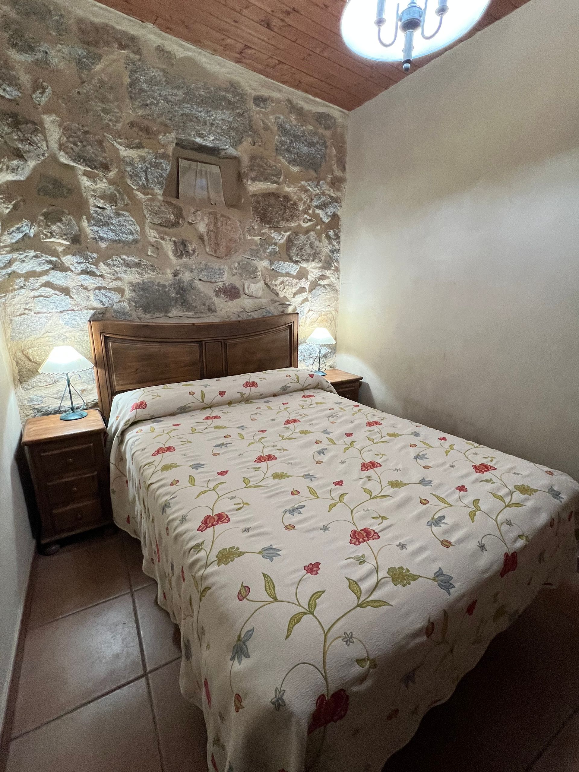 Cozy stone-walled bedroom with a double bed, floral bedspread, and bedside lamps