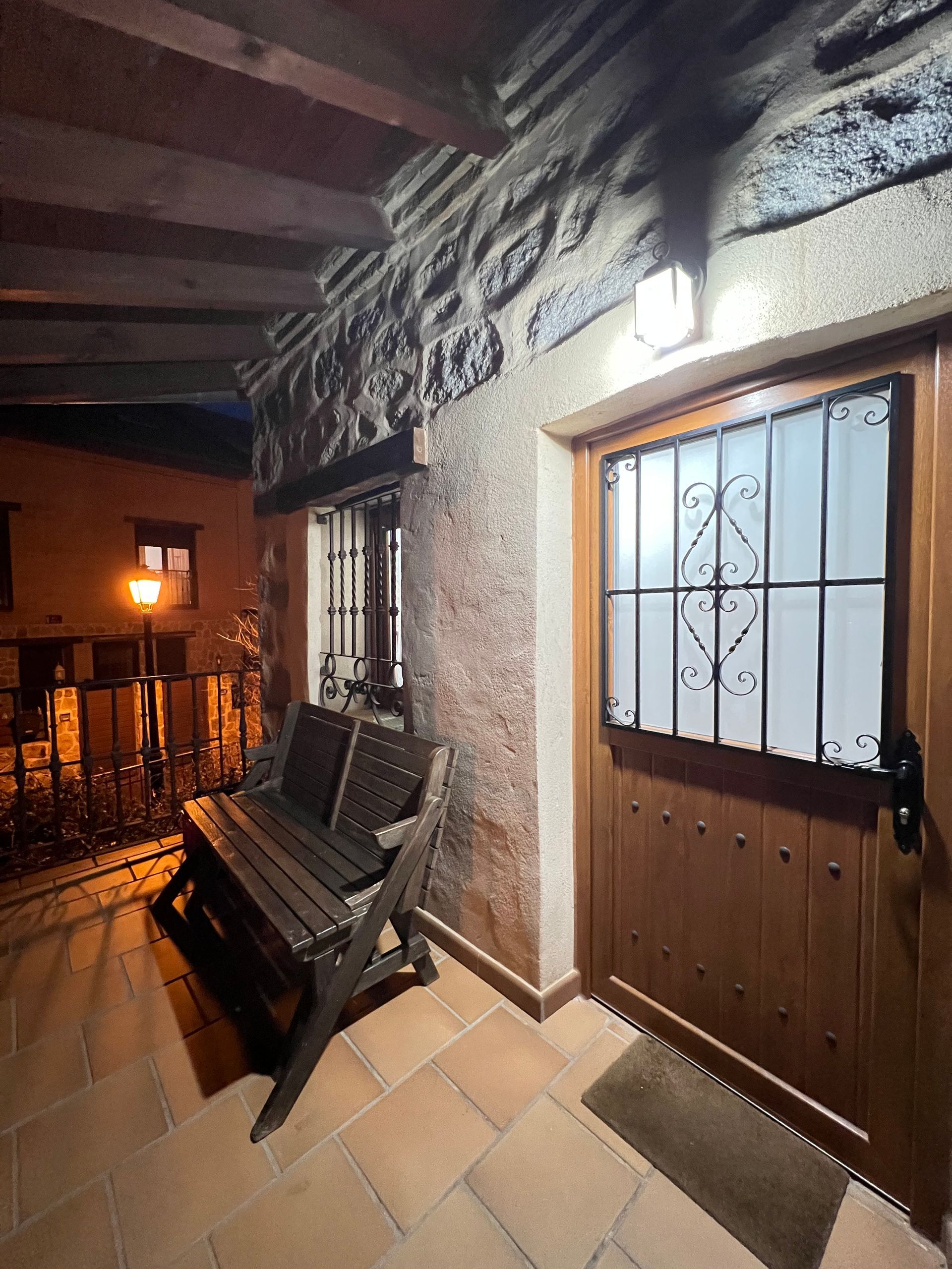 Covered porch with wooden bench, lit lantern, and a brown door at night.