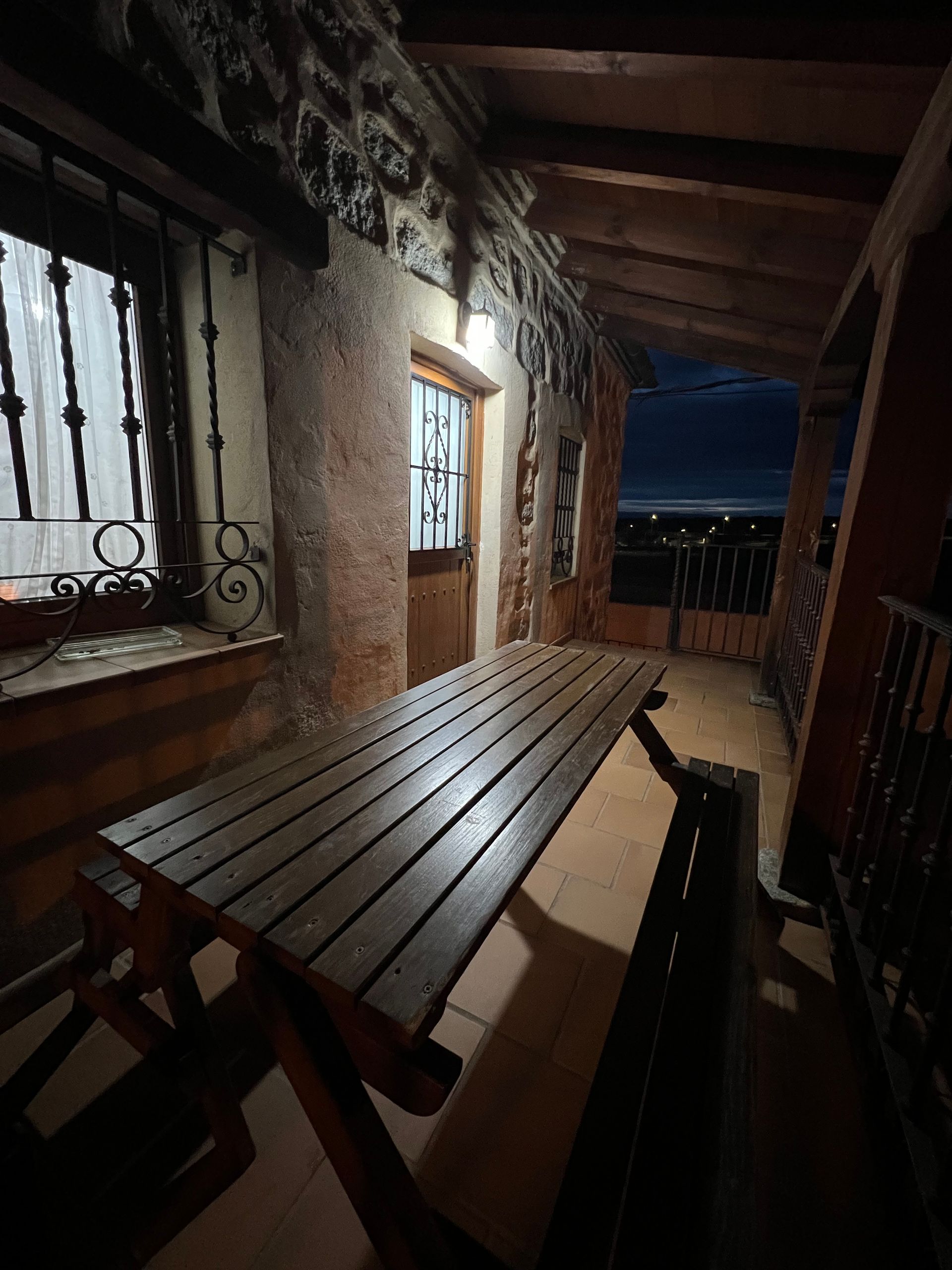 Covered outdoor patio with wooden table and benches, tiled floor, and a view of the dark evening sky.