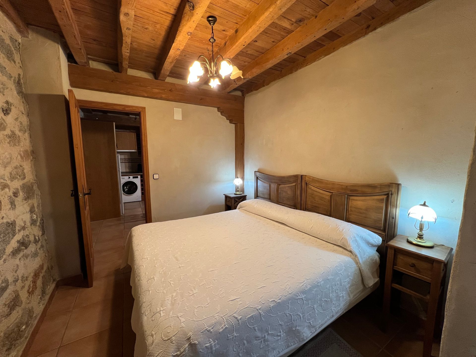 Rustic bedroom with wooden beams, queen bed, nightstands, and warm bedside lamps