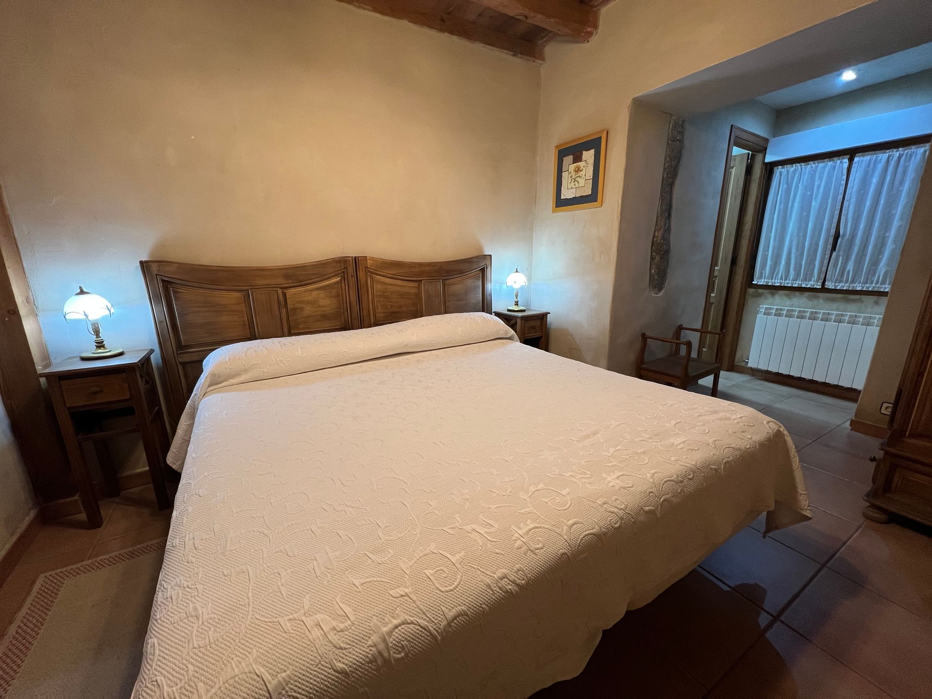 Cozy bedroom with a wooden bed, white bedding, bedside lamps, and an adjoining bathroom door open.
