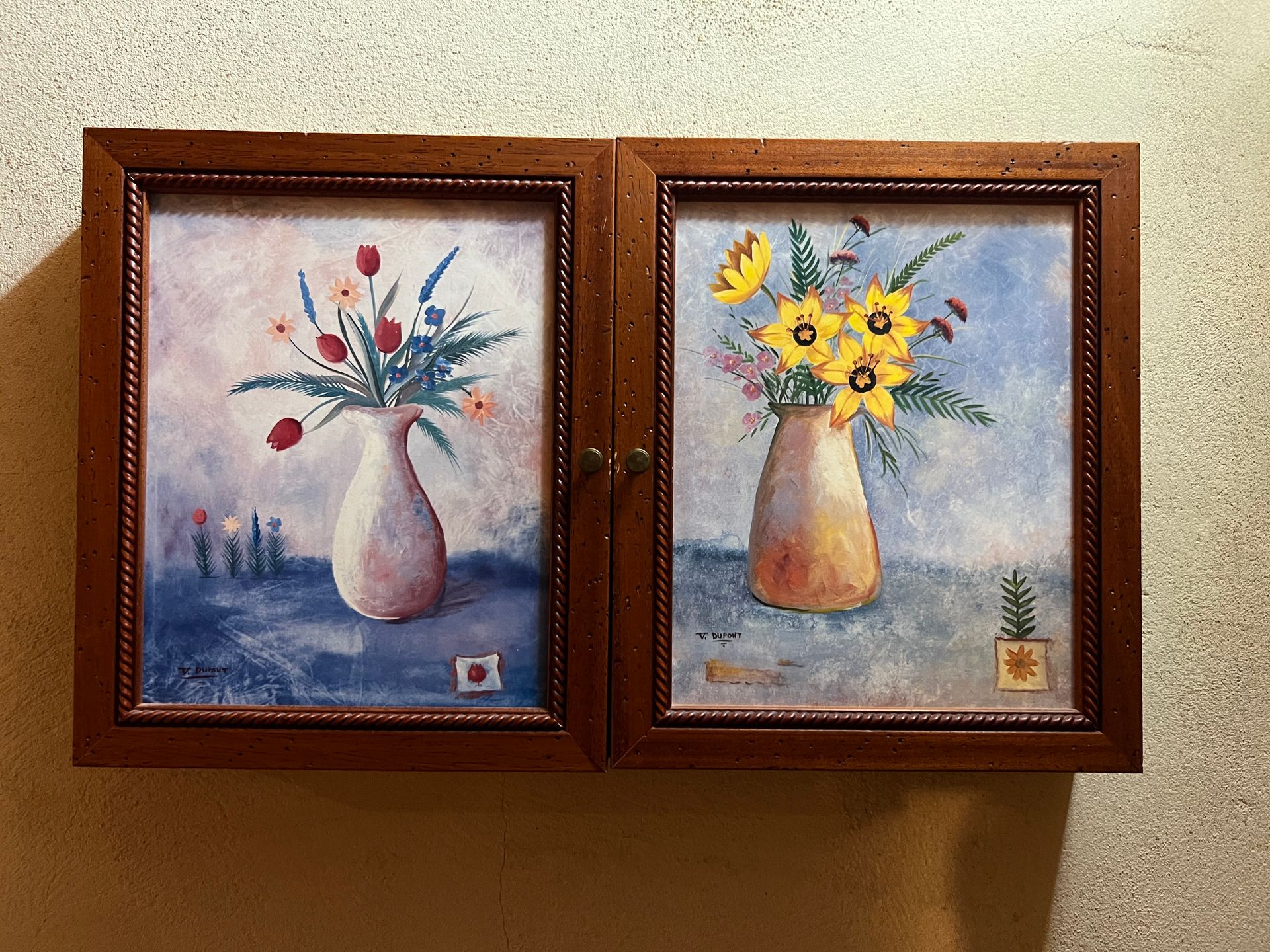 Two framed floral still-life paintings with vases on a beige wall.