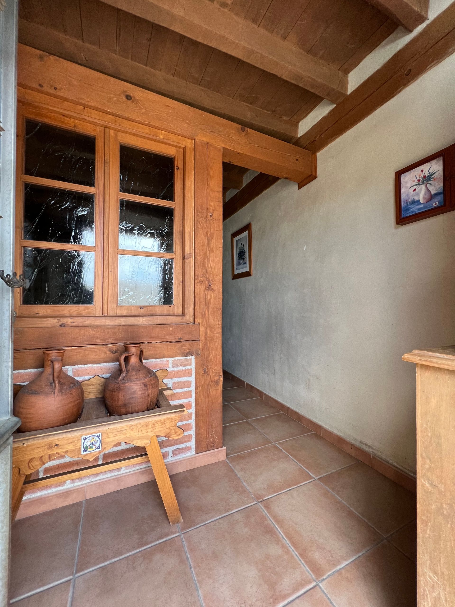 Wooden entryway with tiled floor, terracotta pots on a bench, and a narrow hallway with framed wall art.