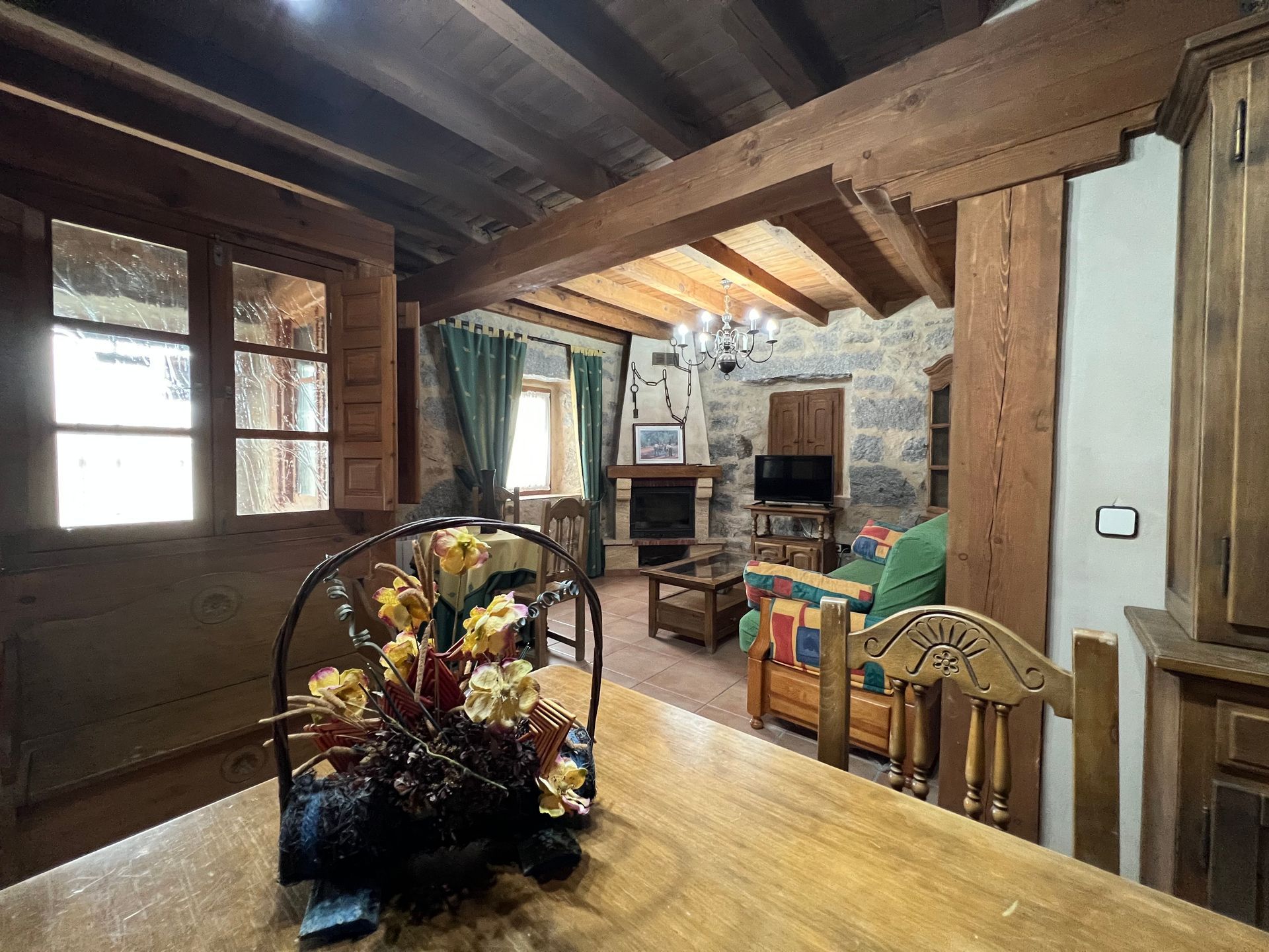 Rustic cabin dining room with wooden beams, stone fireplace, and a table with a floral centerpiece.