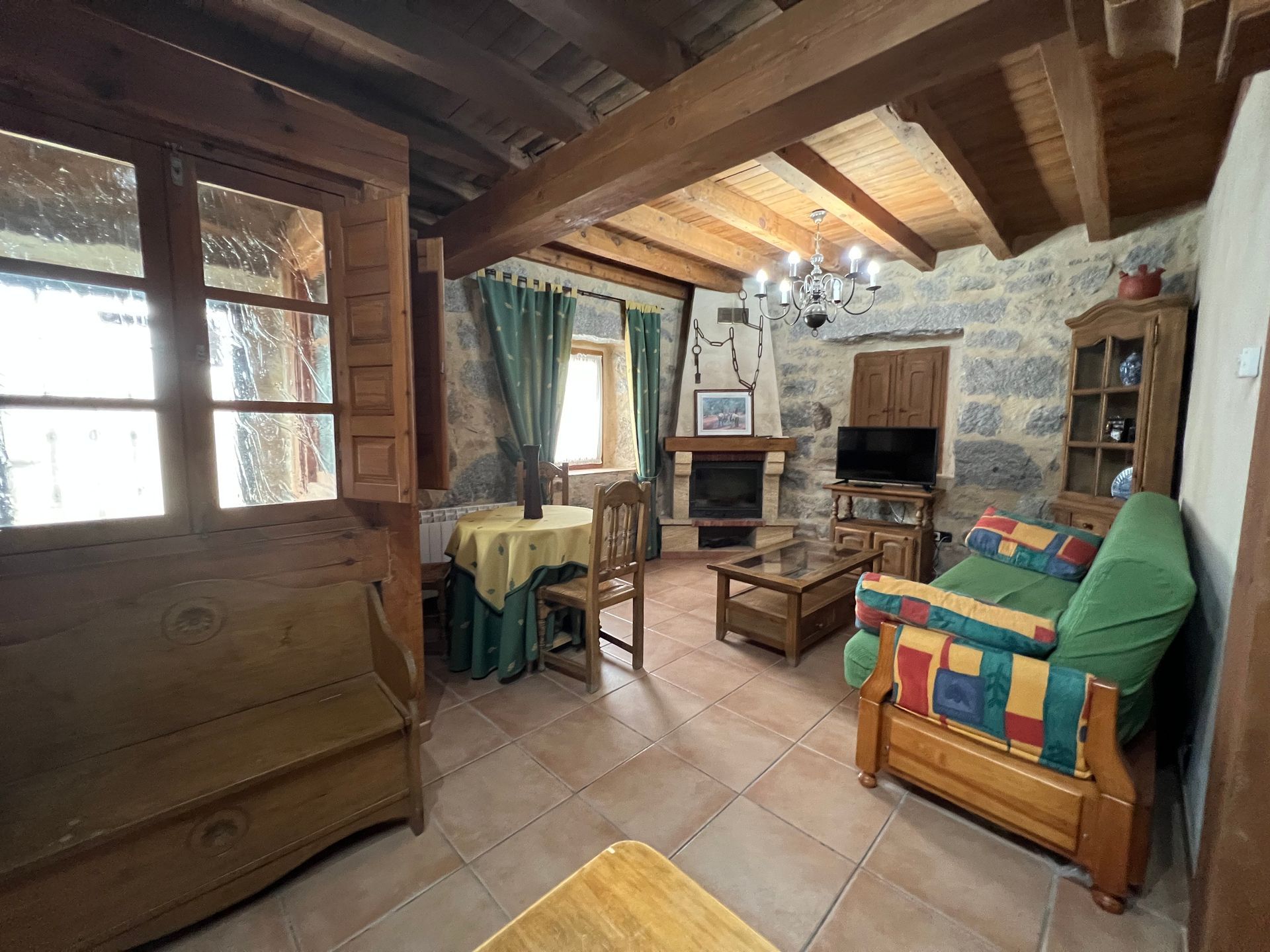 Rustic living room with wood beams, stone fireplace, green sofa, and colorful quilted chair