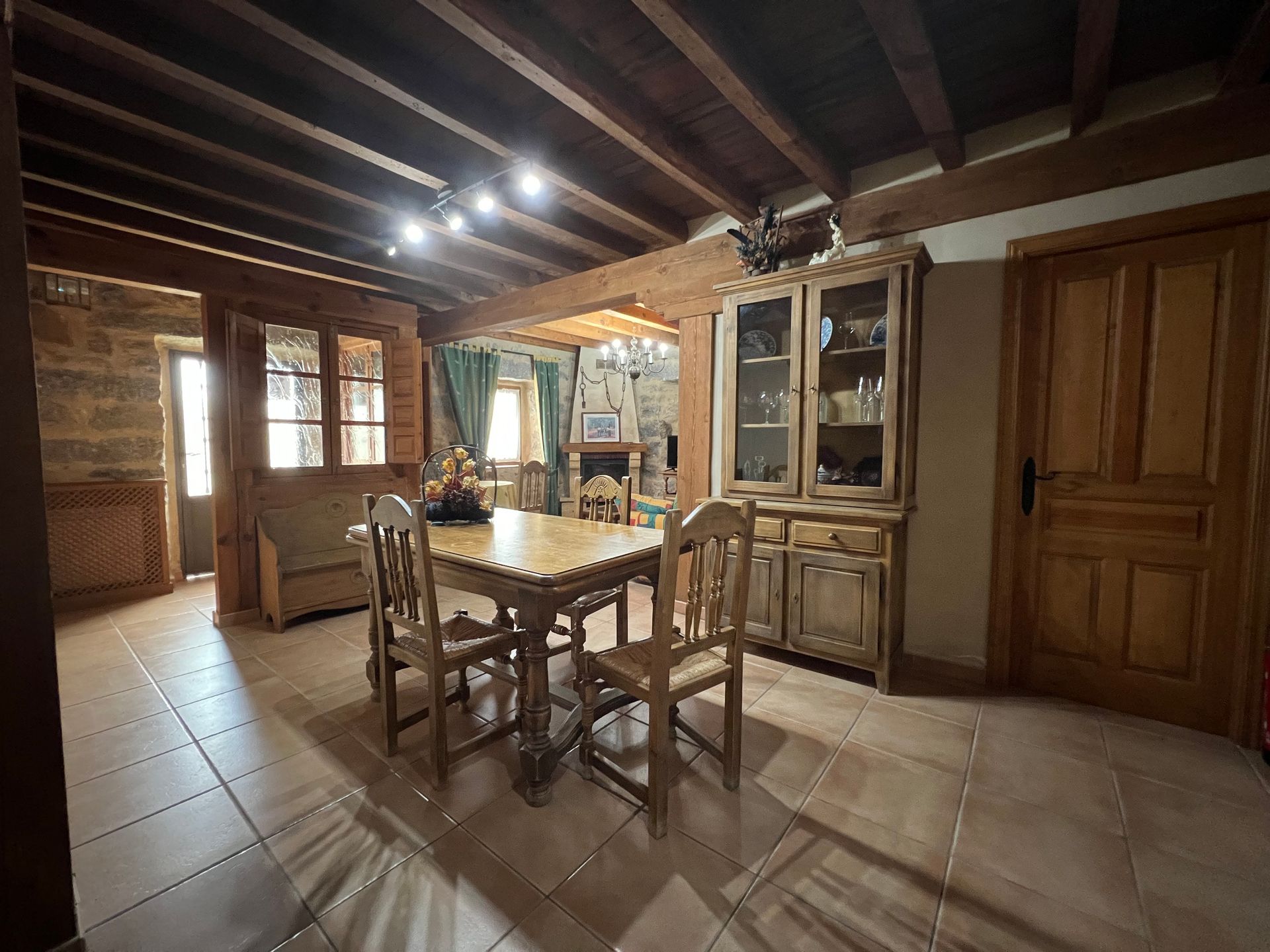 Rustic dining room with wooden table and chairs, exposed beams, tiled floor, and large cabinet.