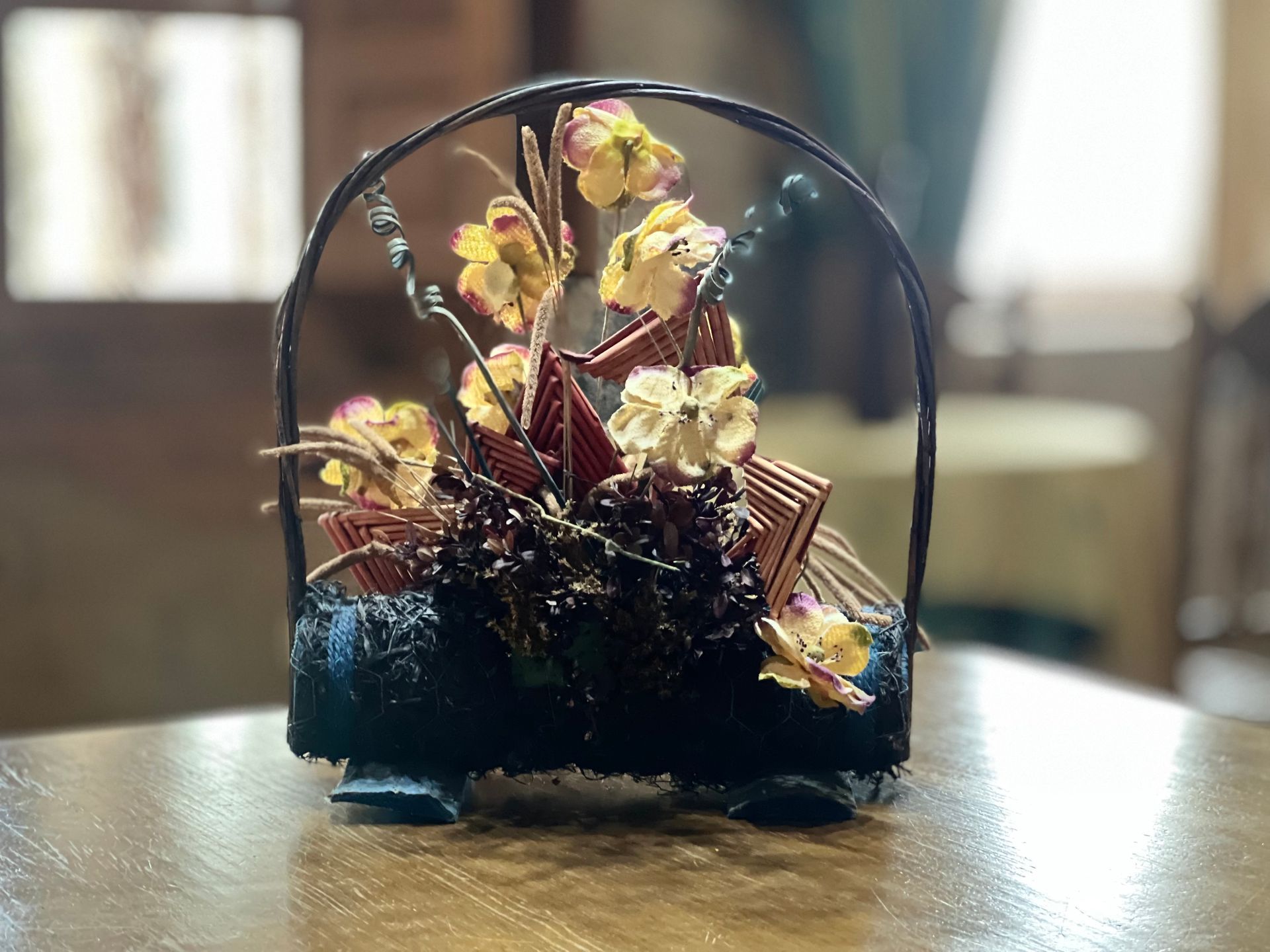 Small floral arrangement with yellow and pink flowers in a glass dome on a wooden table