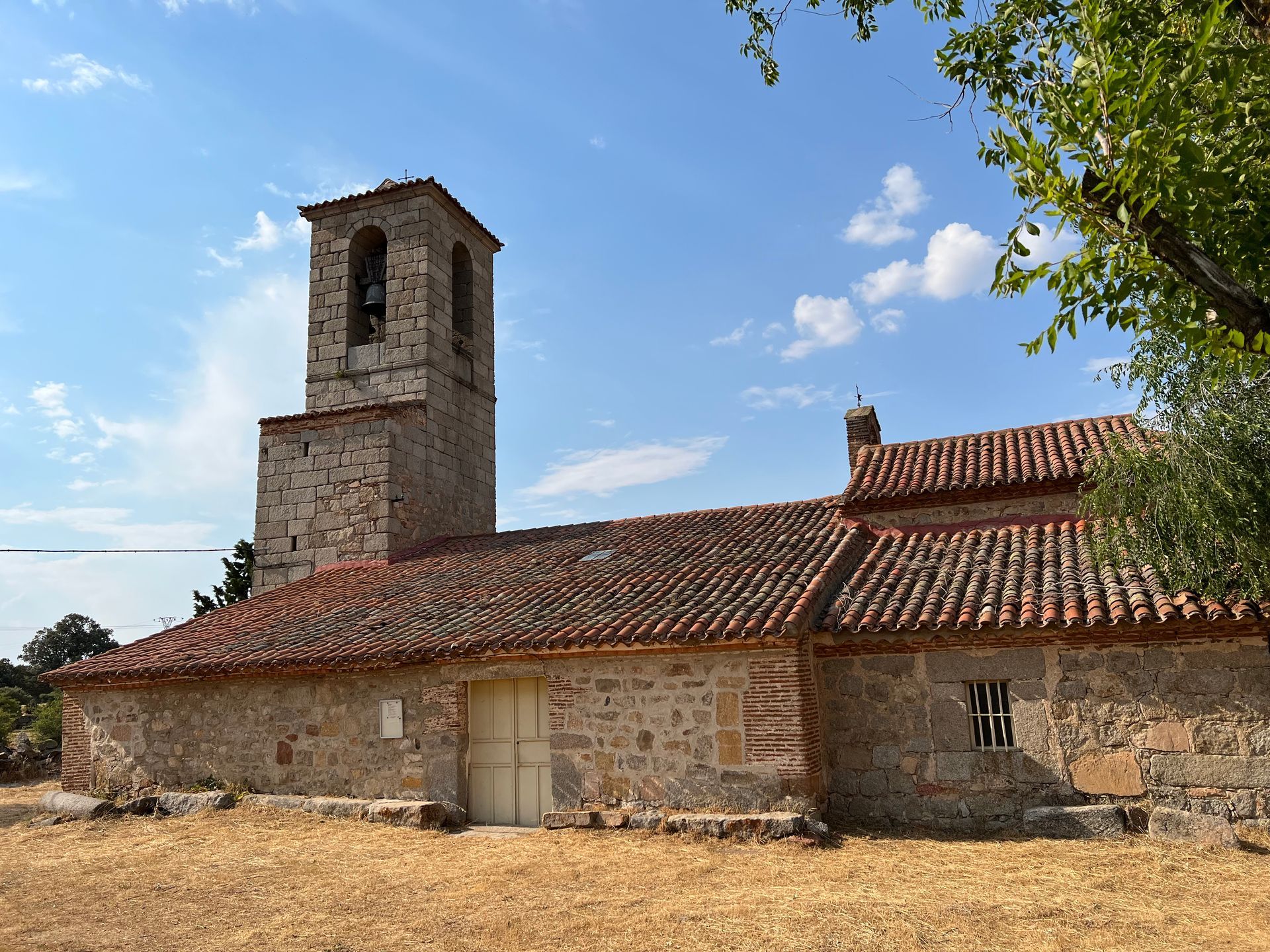 Old stone church with a tiled roof and bell tower under a bright blue sky