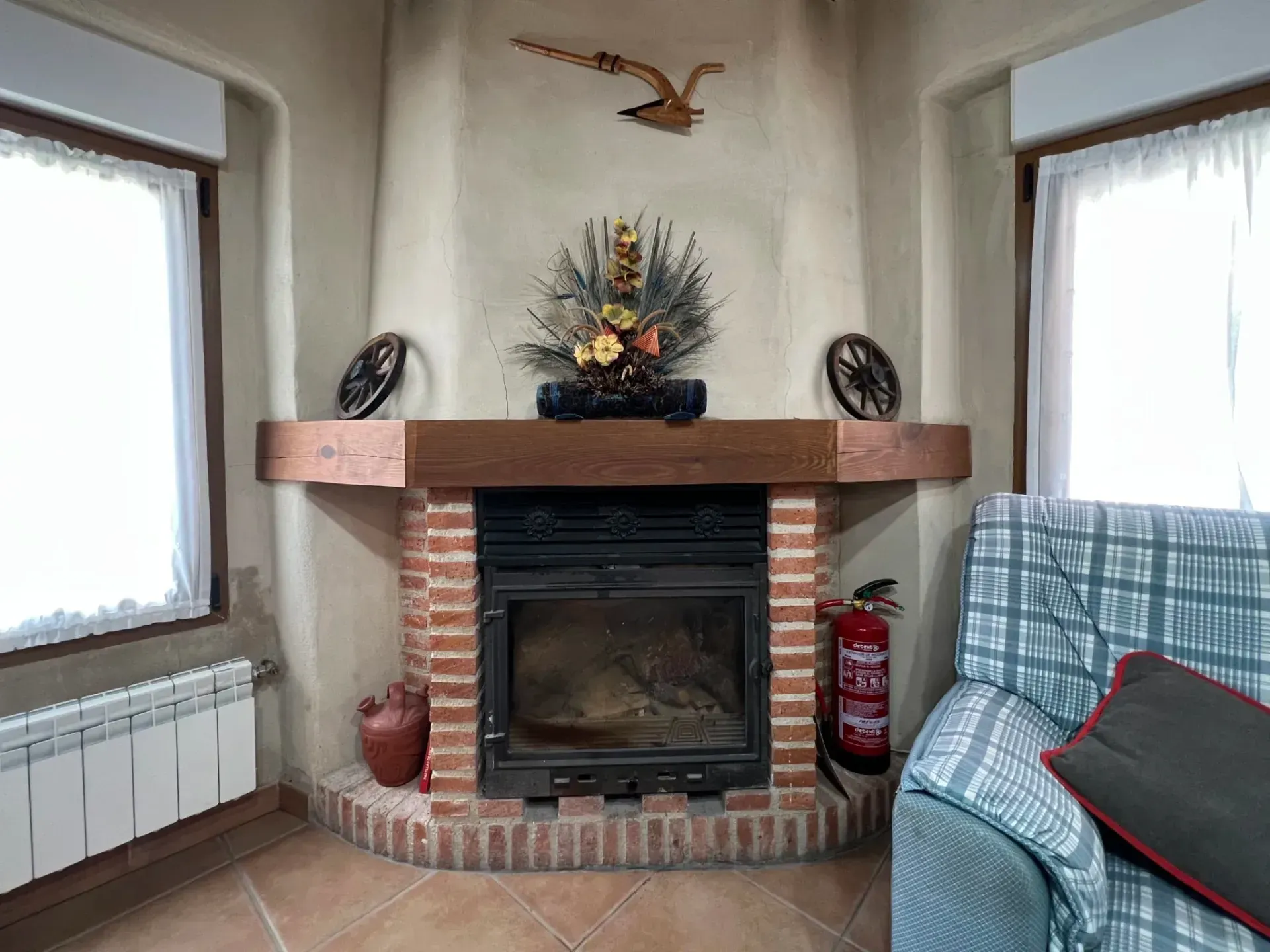 Cozy living room fireplace with brick hearth, wood mantel, birds, and a plaid-covered sofa by a window