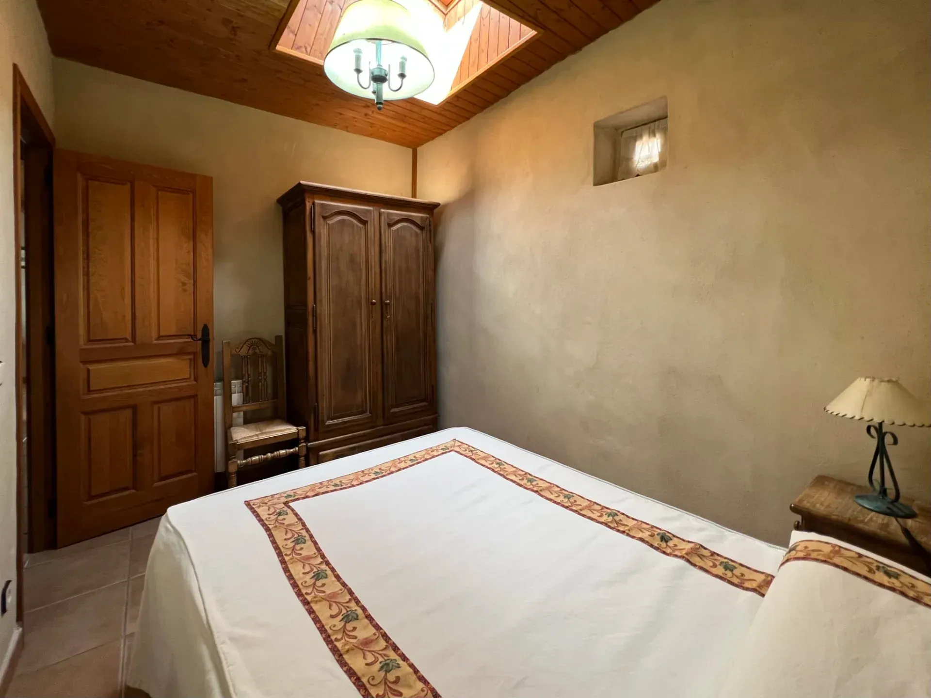 Small bedroom with a bed, wooden wardrobe and door, beige walls, and a ceiling light.