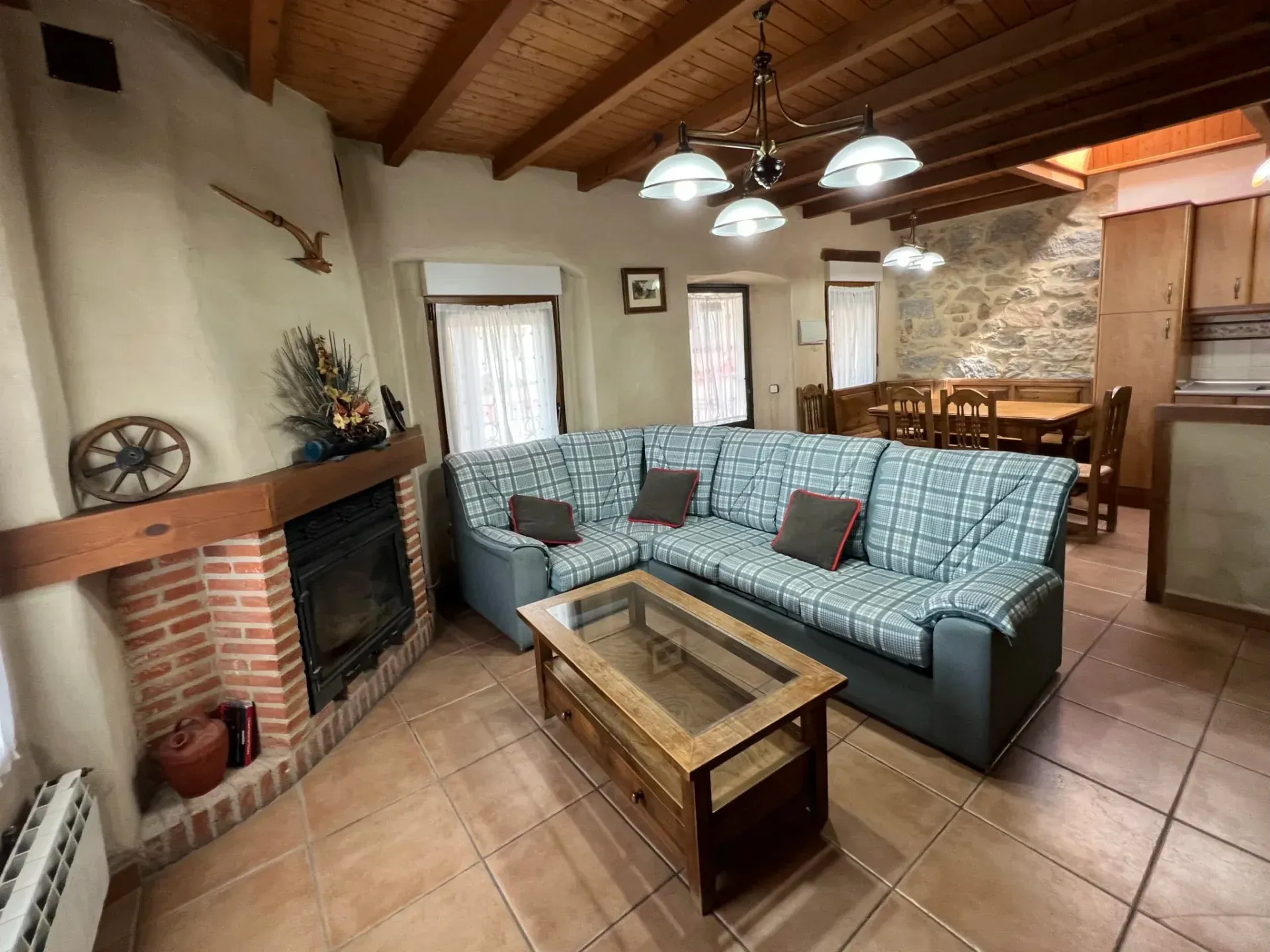 Cozy living room with teal sectional, coffee table, brick fireplace, tiled floor, and wooden vaulted ceiling