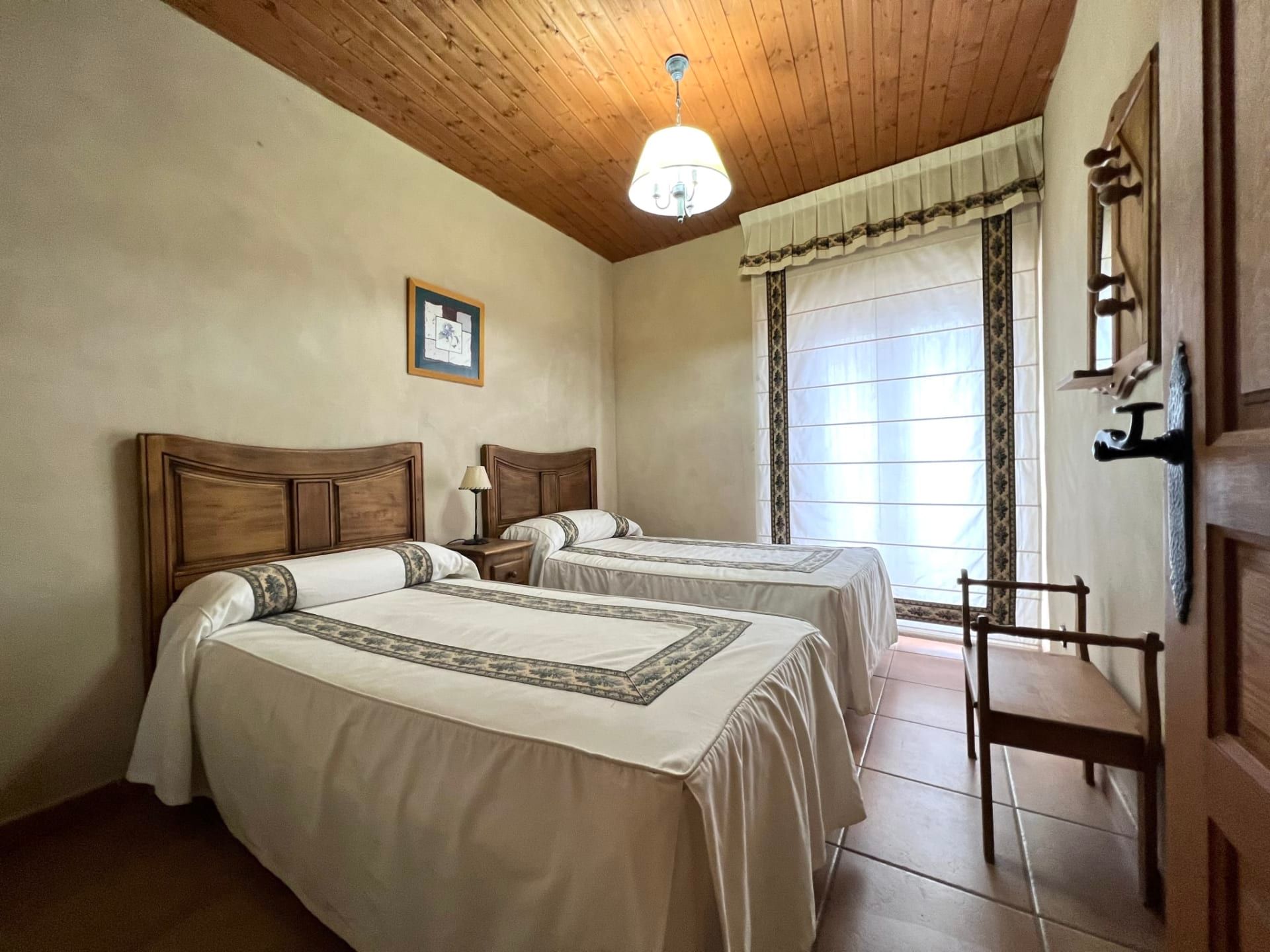 Small bedroom with two twin beds, wood ceiling, and a window with sheer curtains.