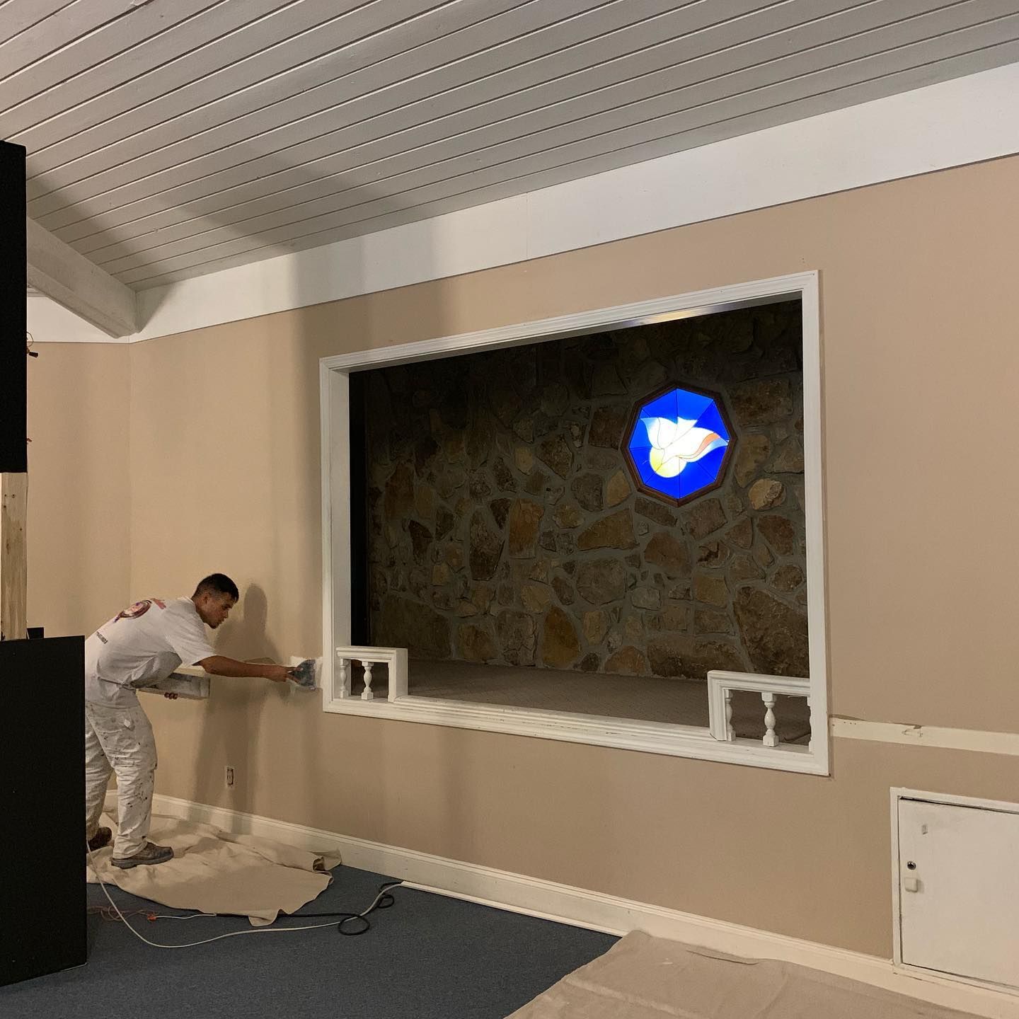 A man is painting a wall in a room with a window.