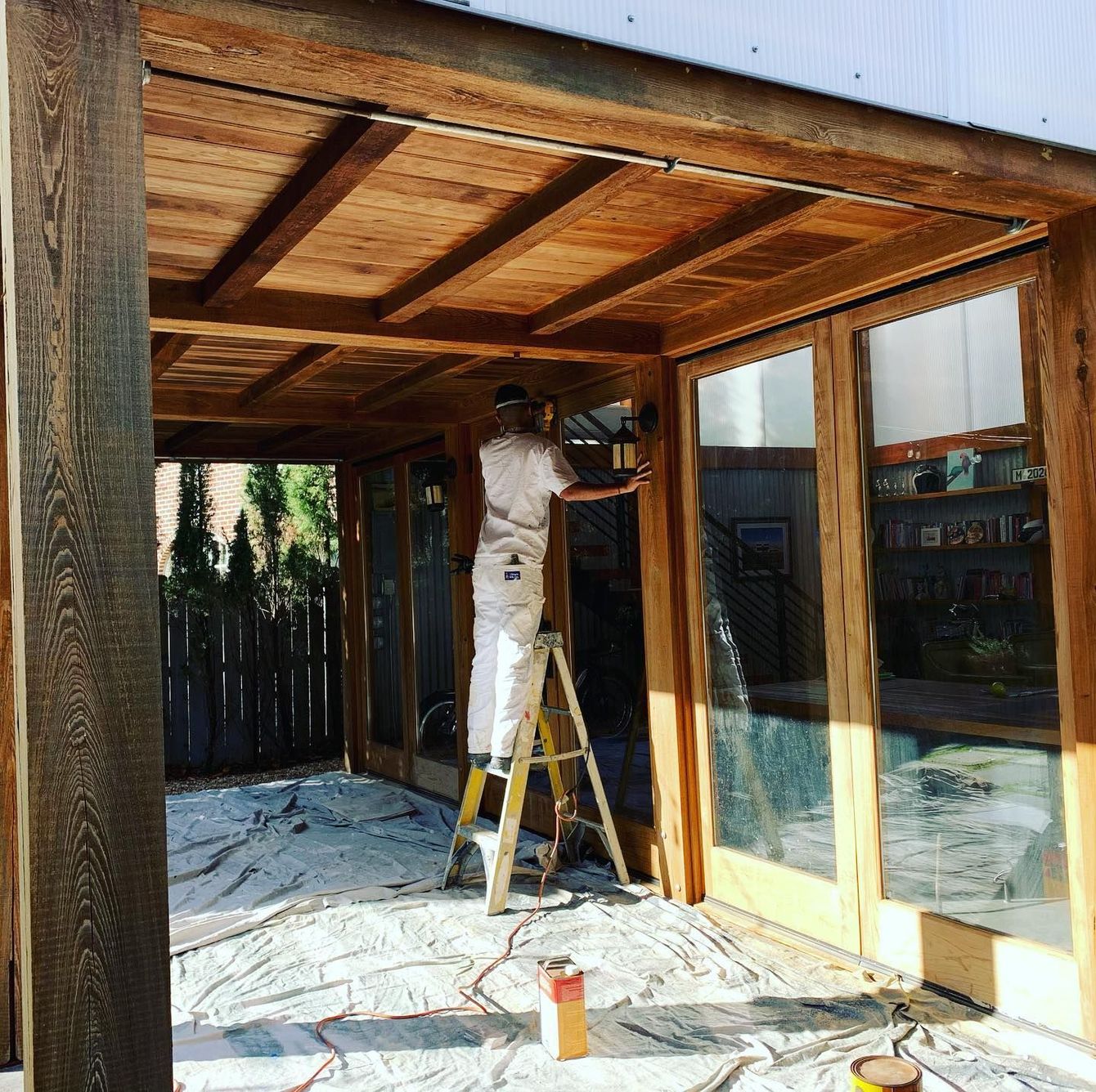 A man standing on a ladder painting a wooden structure