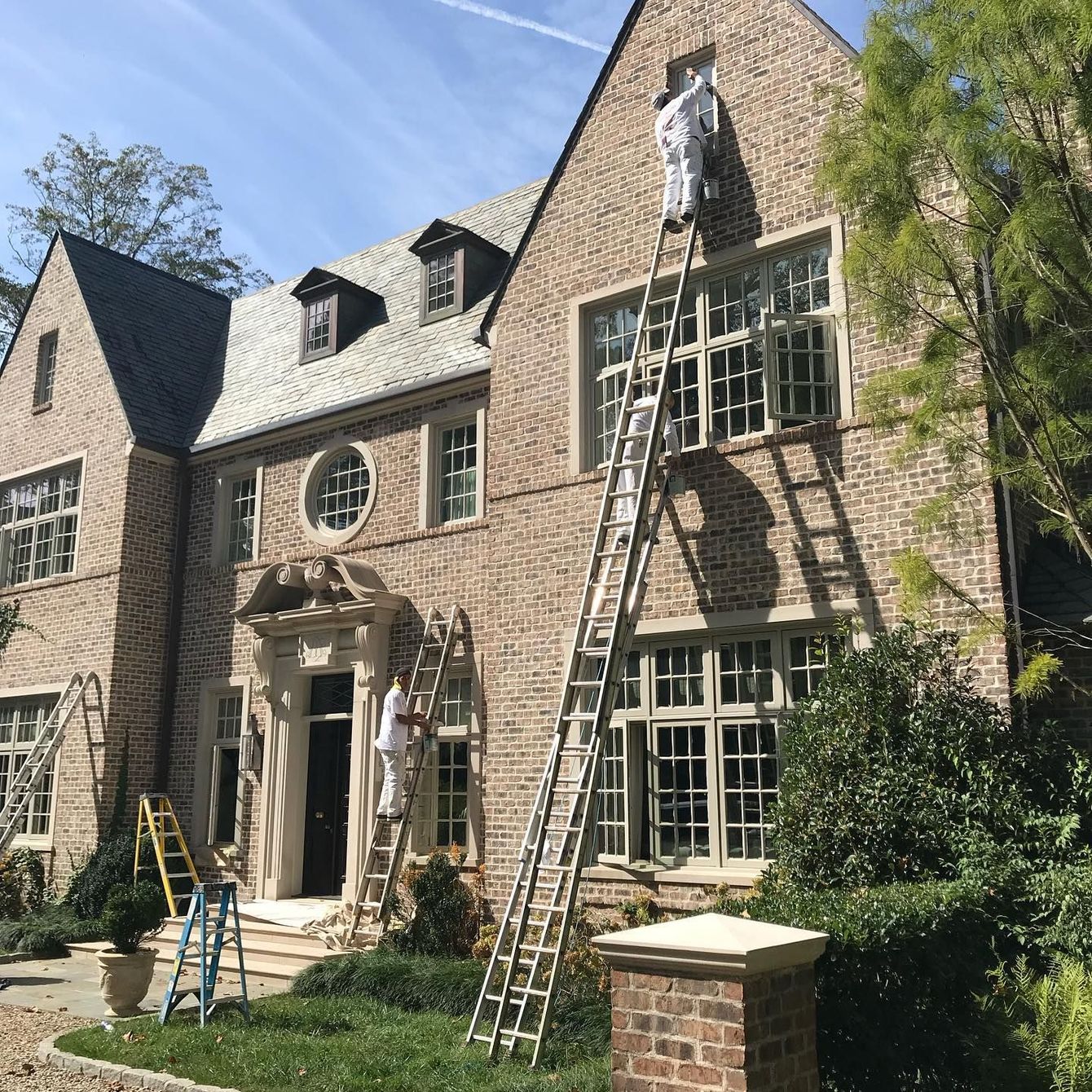 A man is standing on a ladder painting a brick house.