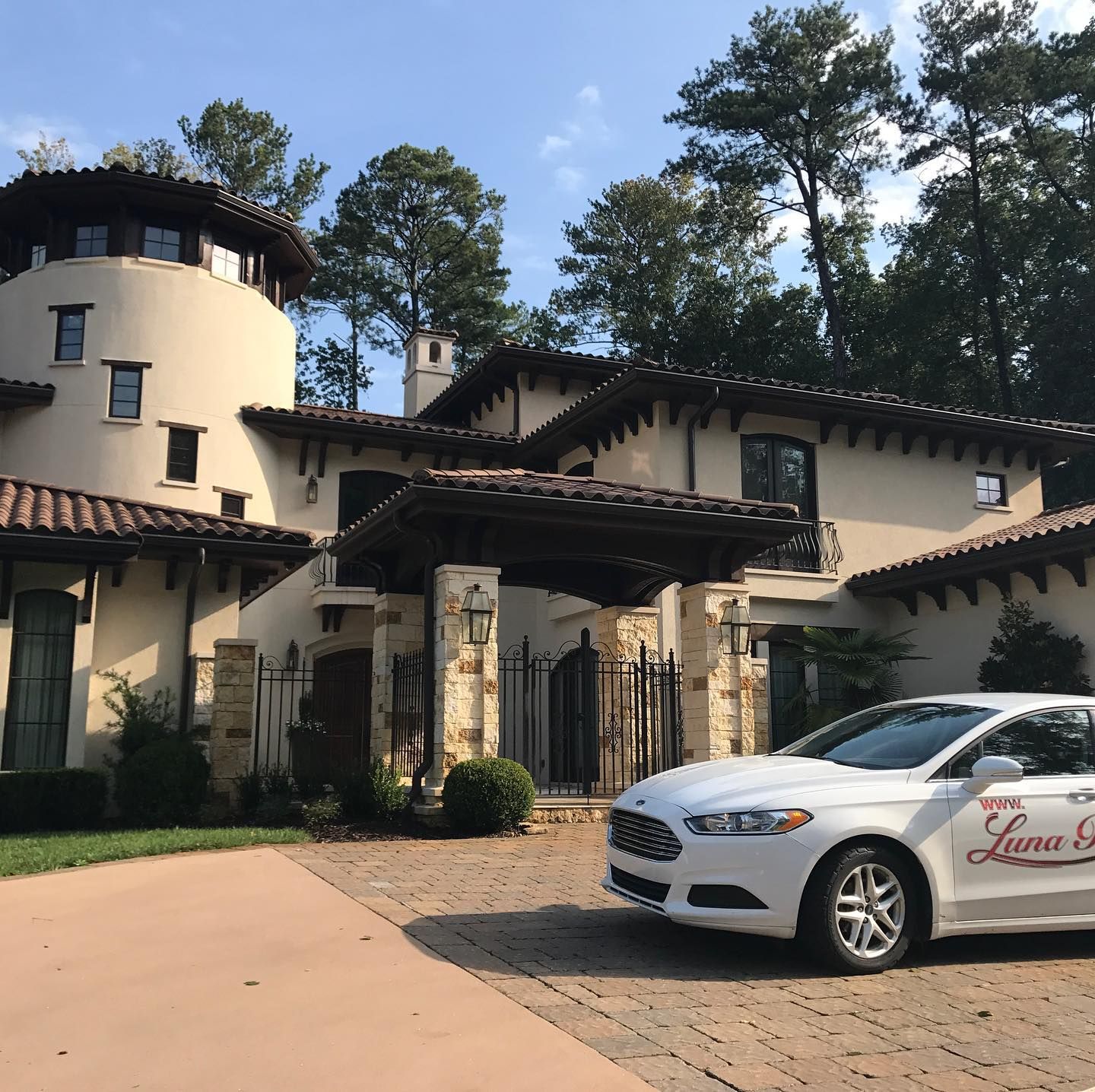 A white car is parked in front of a large house