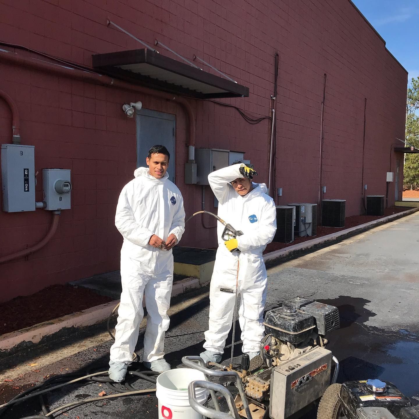Two men in white suits are standing in front of a red building.