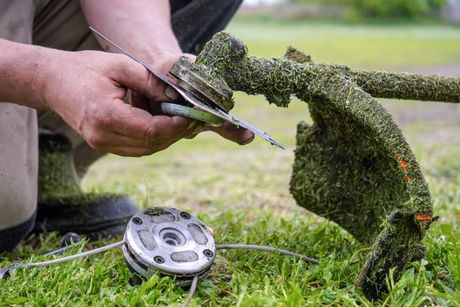 A person holding a metal blade while repairing a grass trimmer in an outdoor setting.