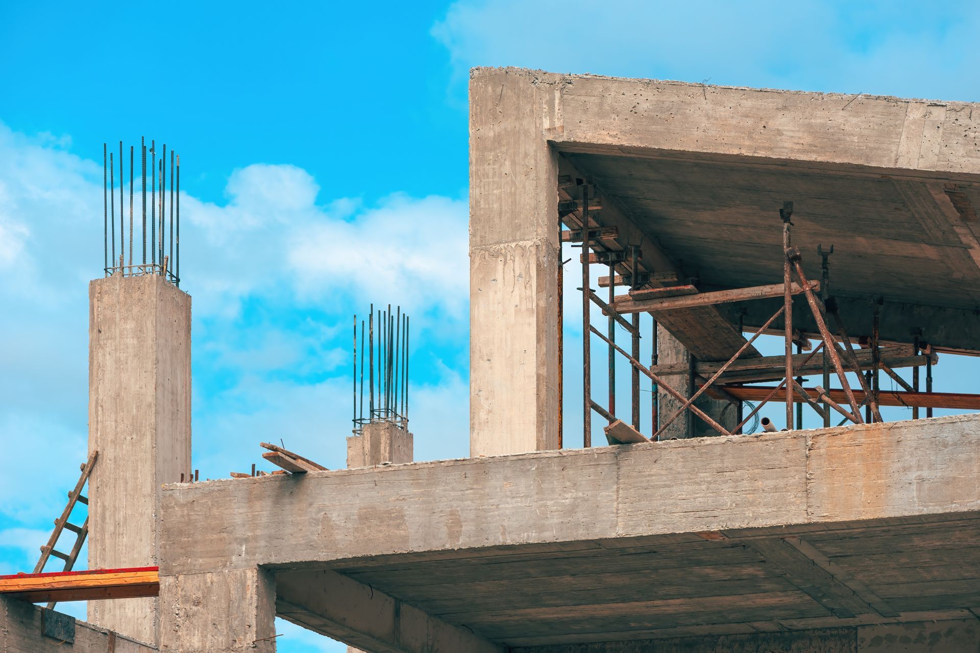 A concrete building under construction with exposed rebar, scaffolding, and a blue sky in the background.