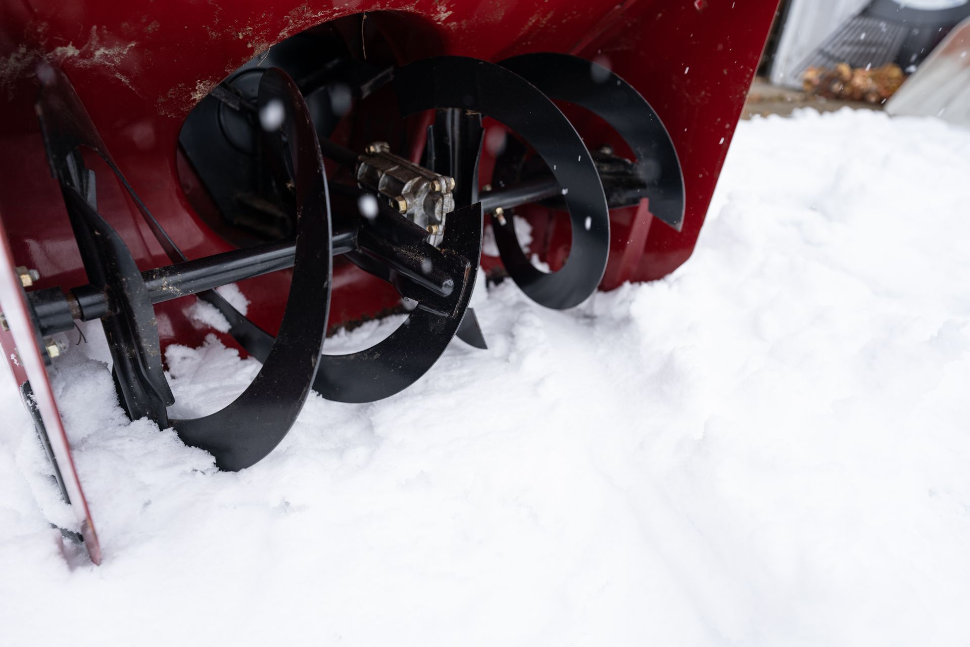 A red snowblower's black metal auger rests in deep white snow.